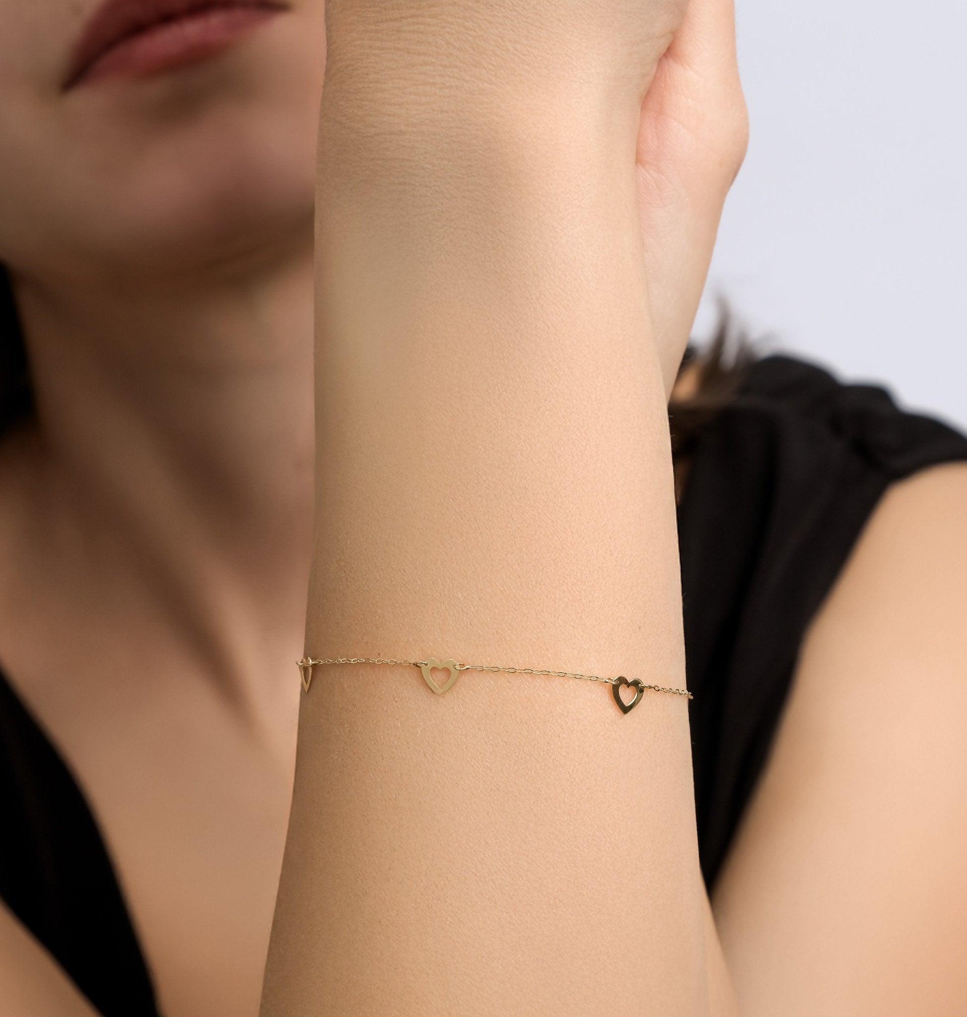 14K solid yellow gold small heart station bracelet worn on a woman's wrist, featuring delicate heart stations.