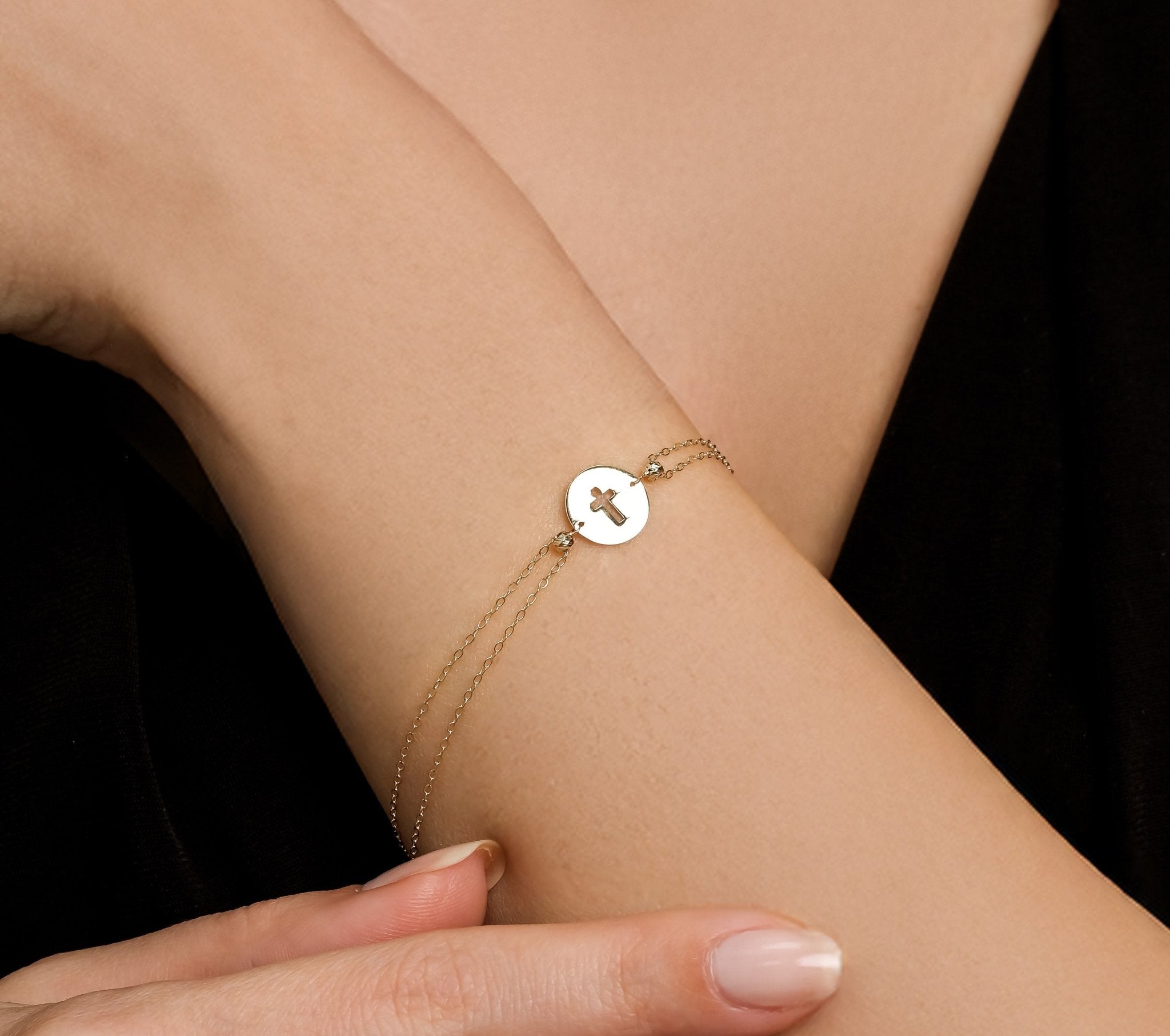 14K solid yellow gold small round disk cross bracelet worn on wrist, showcasing delicate design and dainty chains.