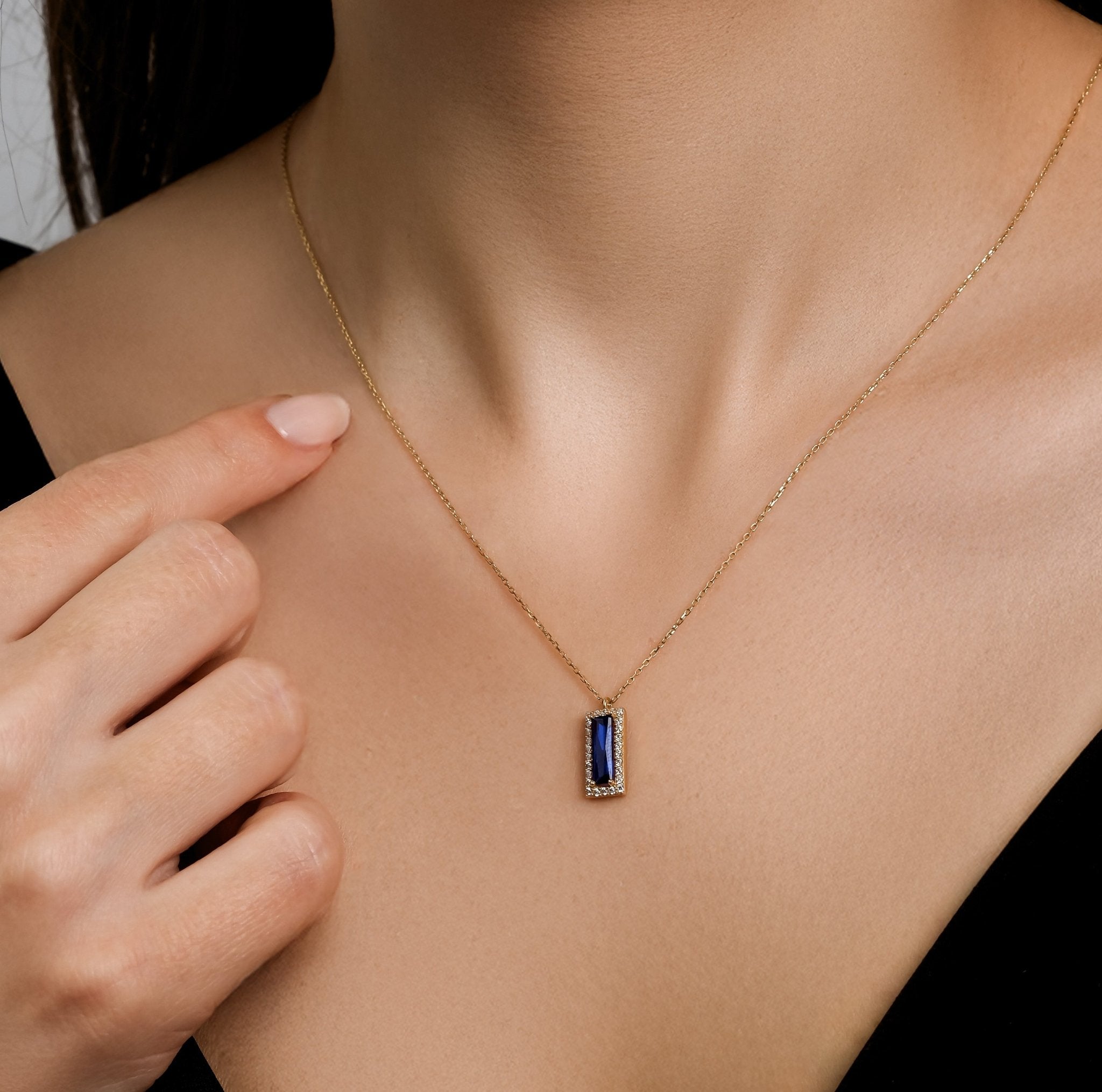 Dainty 14K solid yellow gold solitaire baguette sapphire necklace worn by model, showcasing elegance and simplicity.