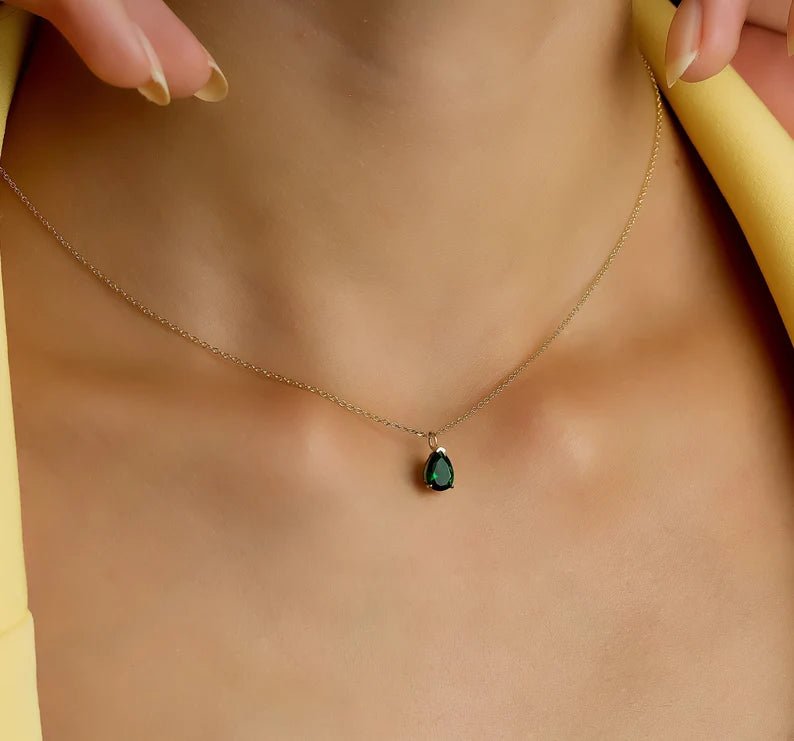 Dainty 14K yellow gold pear shape emerald necklace worn on a model, showcasing the minimalist design.