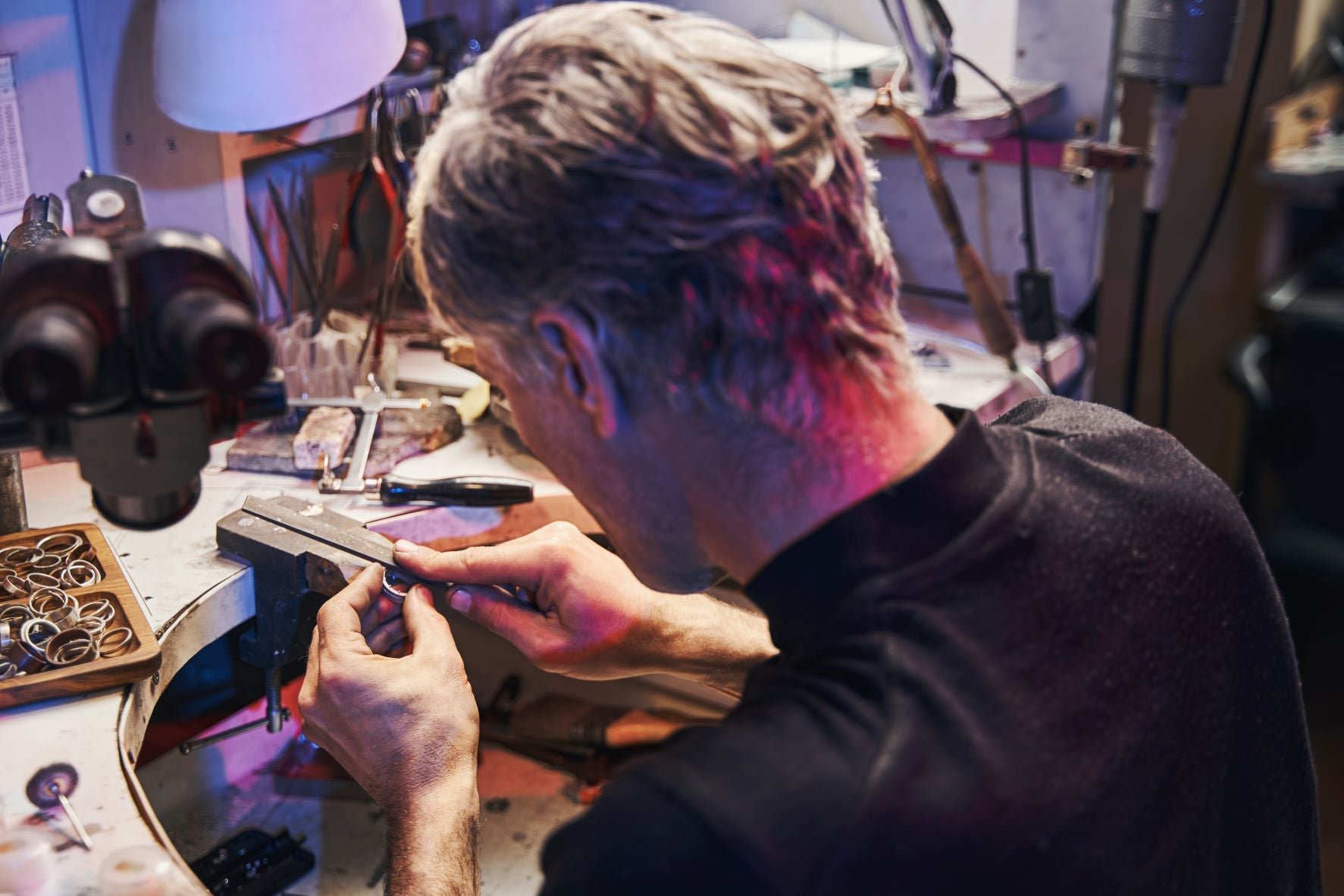 Skilled artisan meticulously crafting jewelry in a well-equipped workshop with various tools and materials.