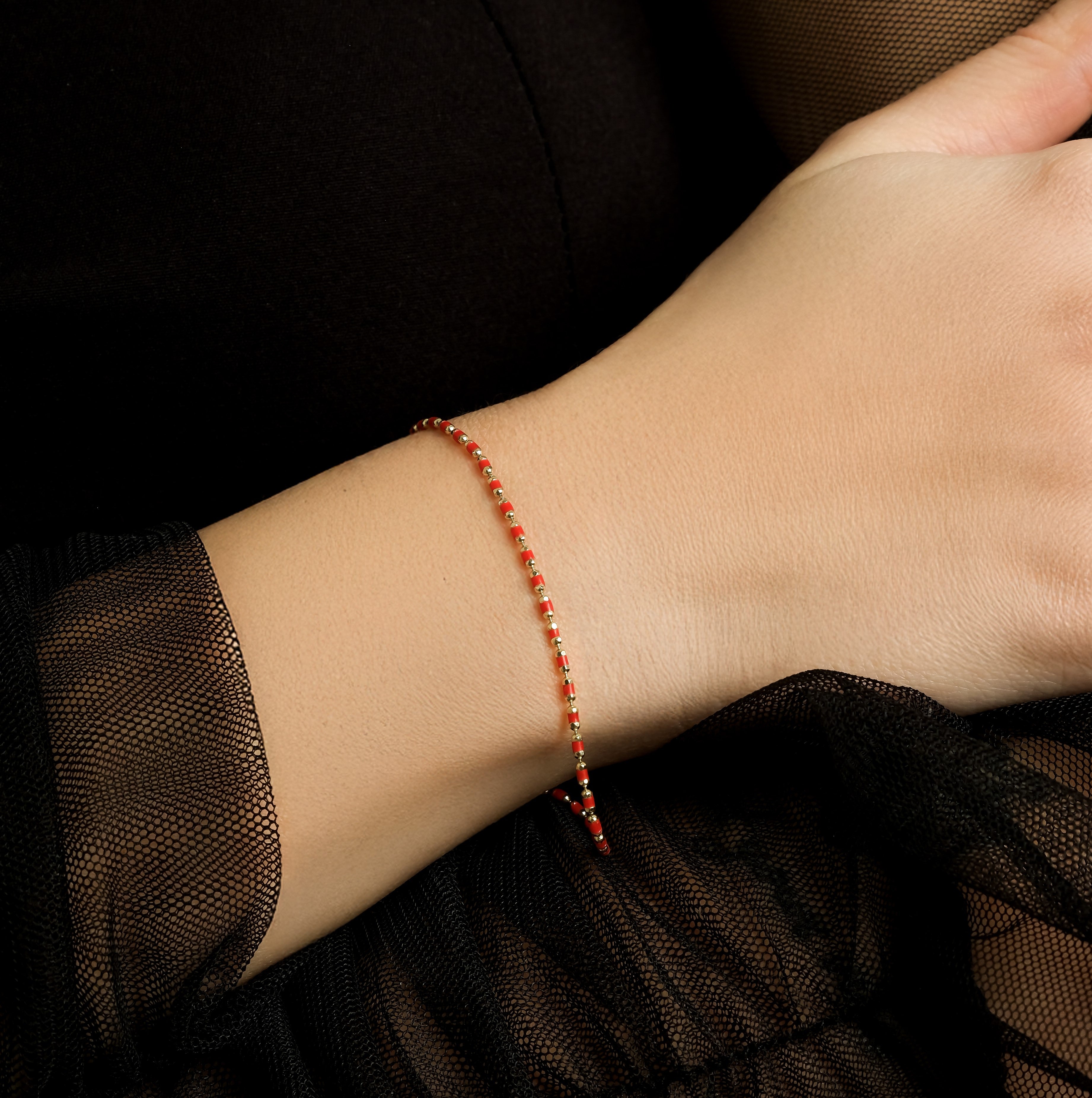 Delicate 14K yellow gold red enamel beaded bracelet worn on wrist, showcasing minimalist design against a stylish outfit.