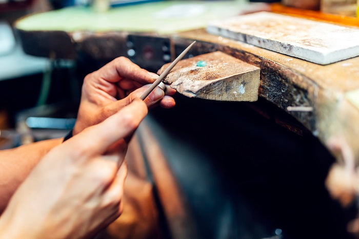Close-up of hands filing wood on a workbench, showcasing artisanal craftsmanship in a workshop setting.