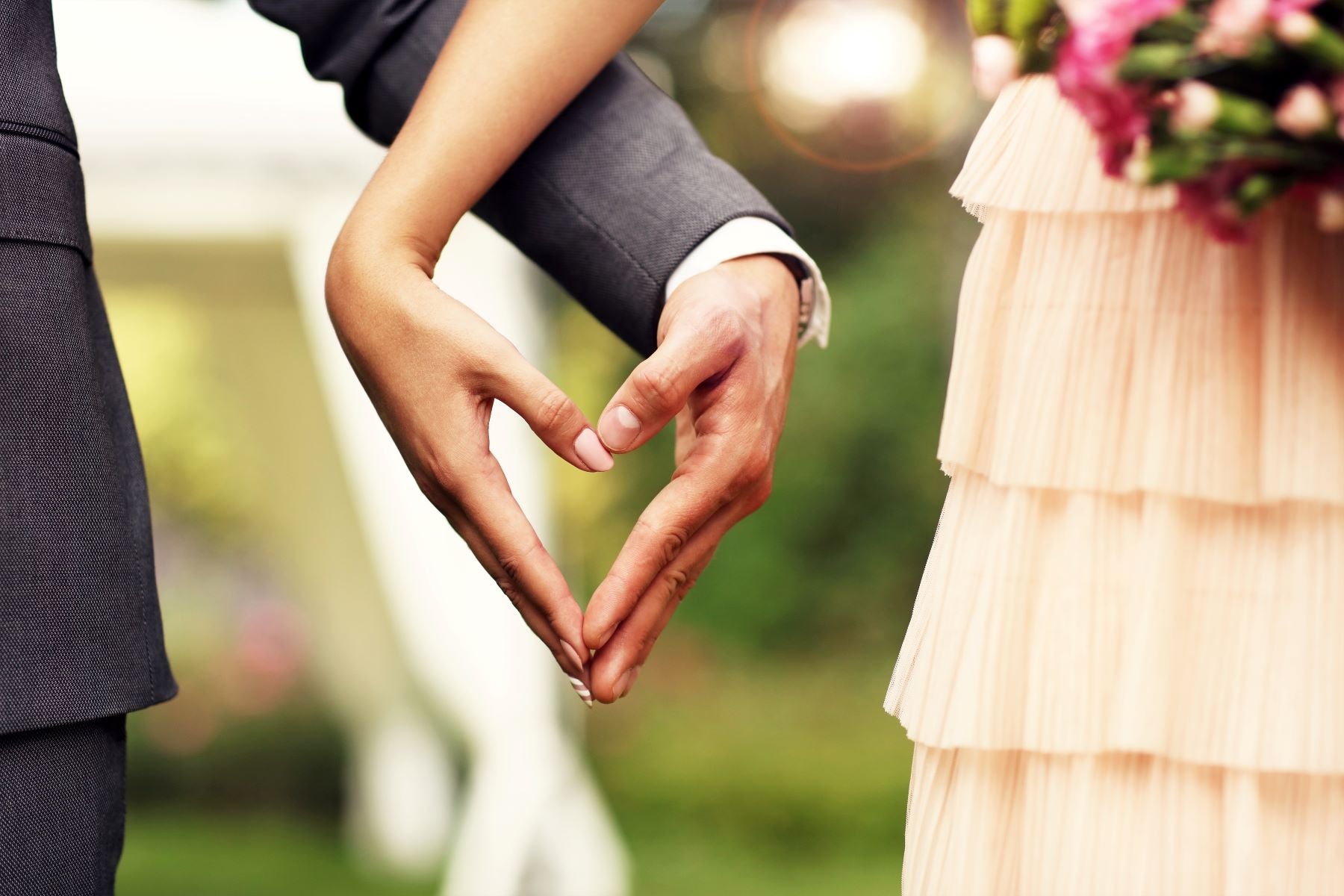Couple forming a heart shape with their hands at an outdoor wedding, symbolizing love and commitment.