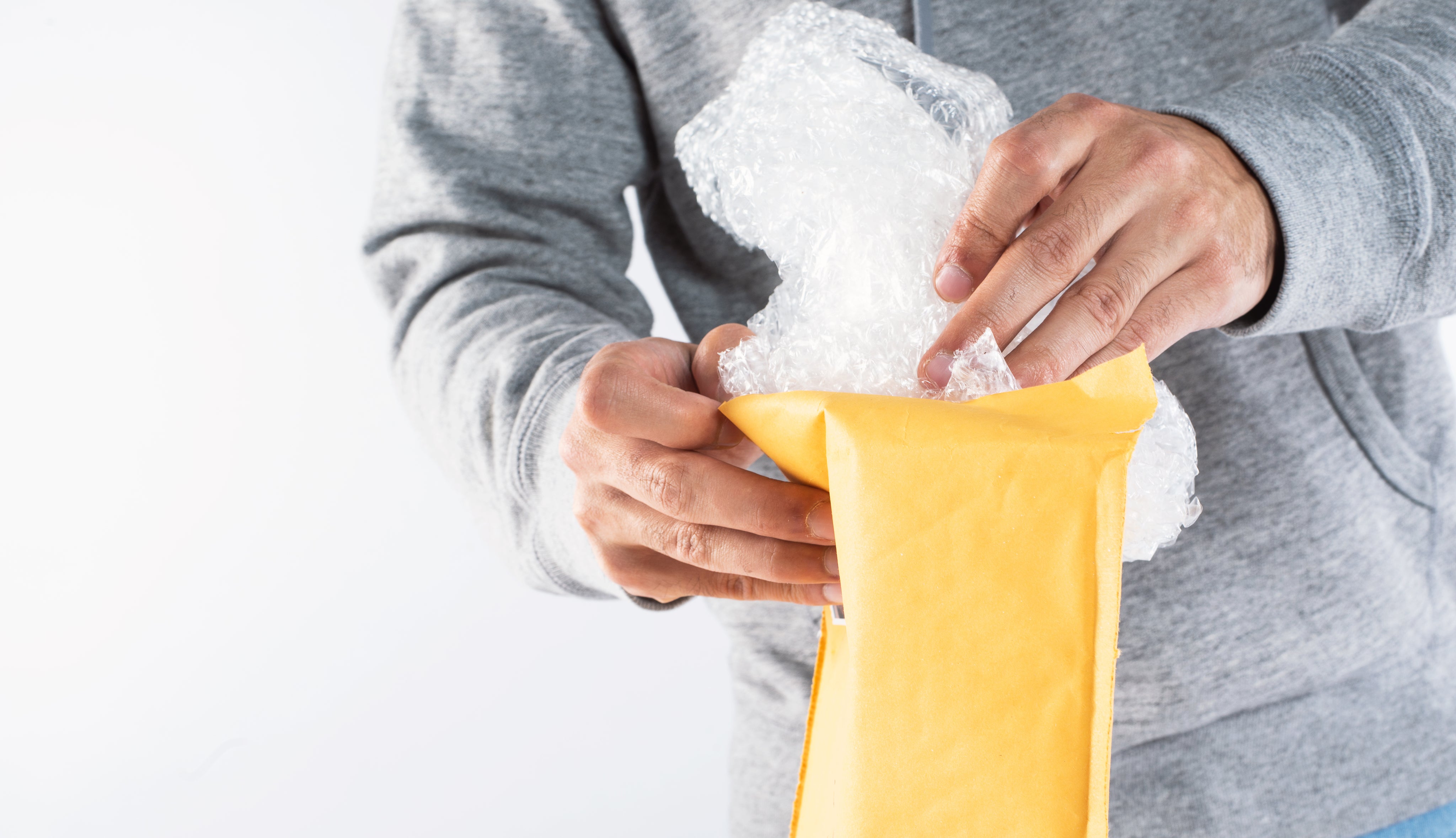 Person unpacking a yellow bubble mailer, carefully removing bubble wrap inside.