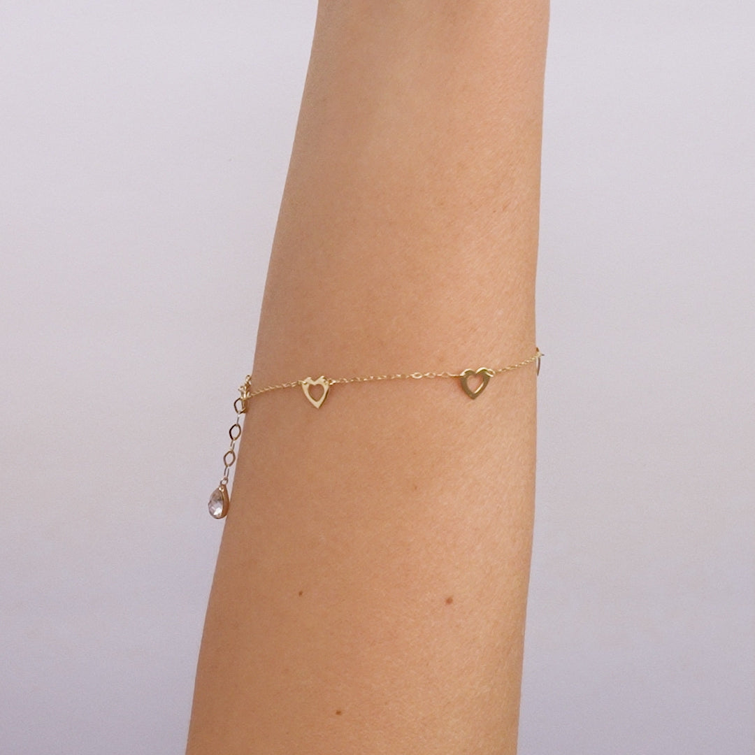 14K solid yellow gold small heart station bracelet on a wrist, featuring delicate heart stations and a dangling charm.