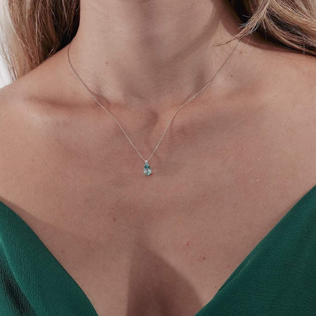 14K white gold solitaire necklace featuring a pear-shaped blue topaz with diamond accents, worn elegantly.