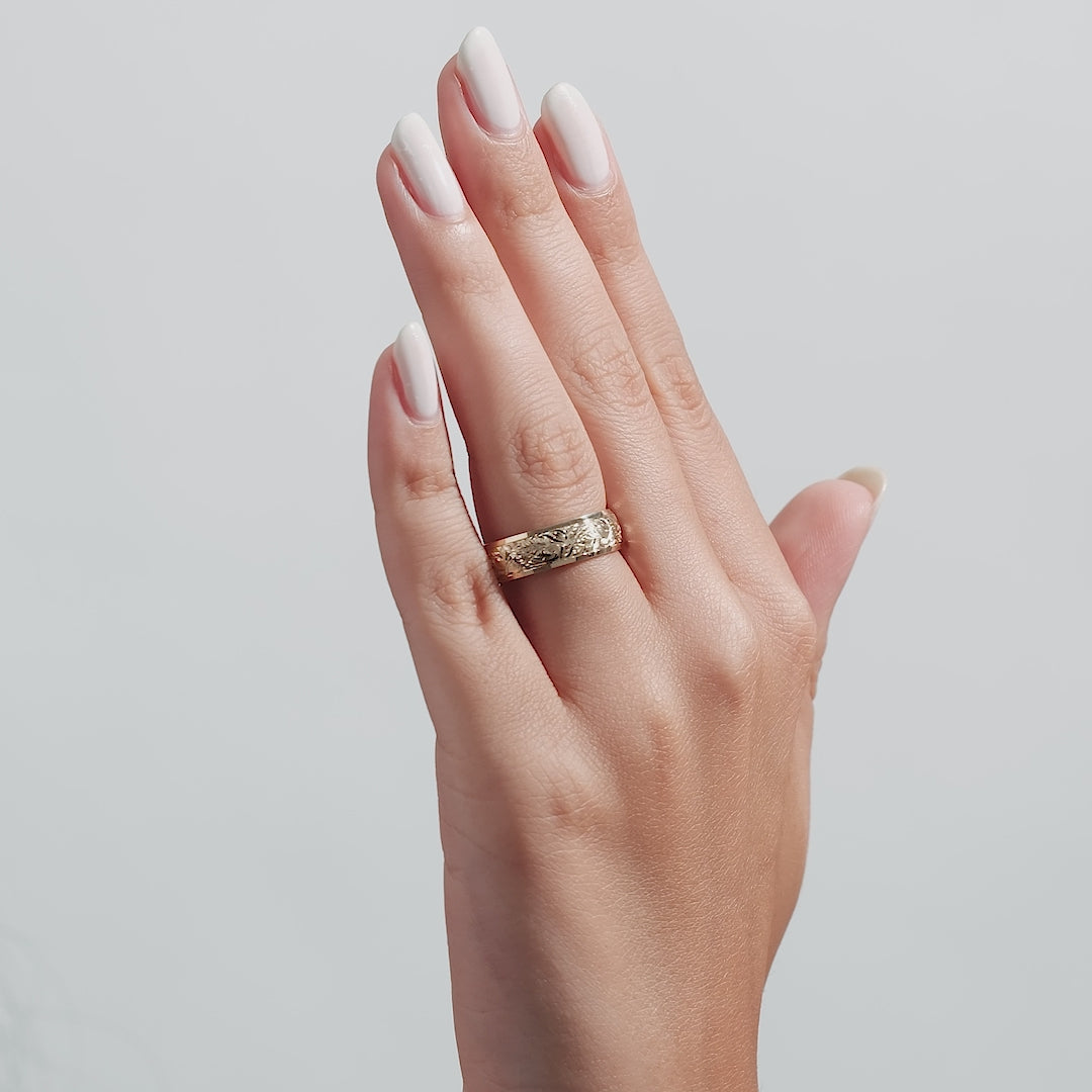 Close-up of a woman's hand wearing a 6mm yellow gold hand engraved wedding ring with leaf motifs.