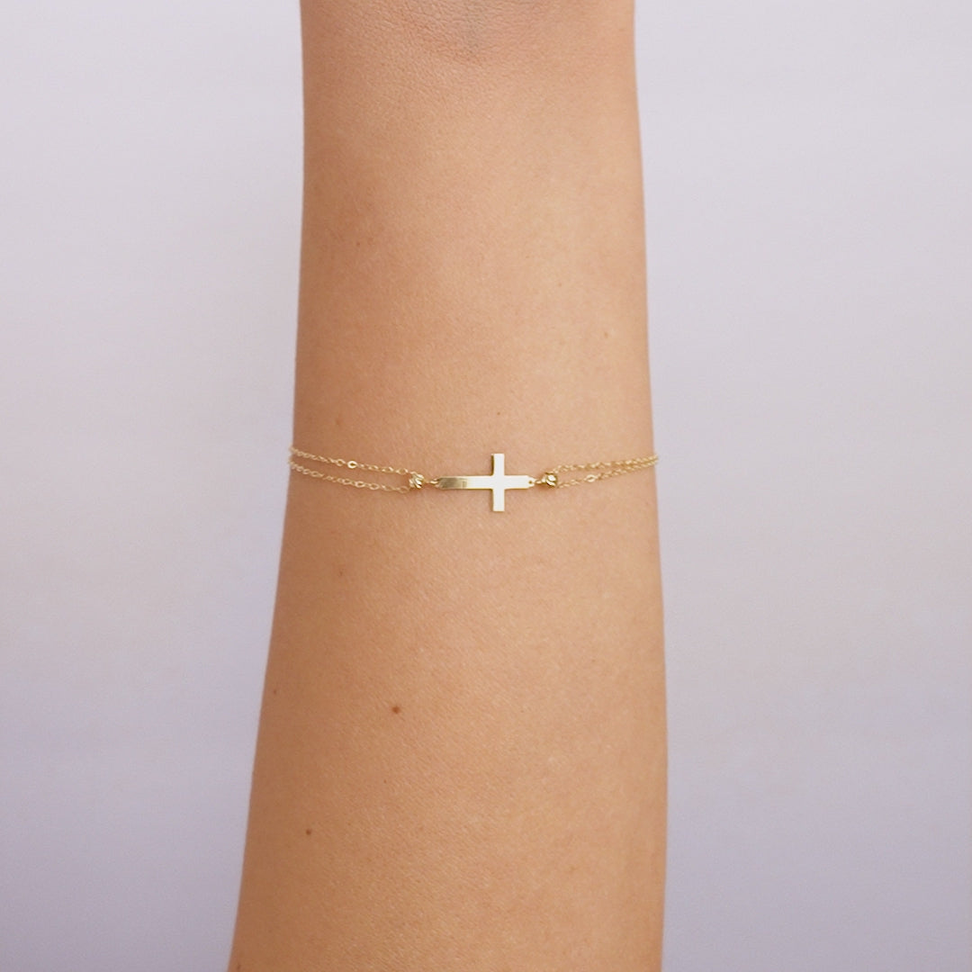 14K solid yellow gold small cross bracelet worn on arm, delicate design, perfect for everyday use.