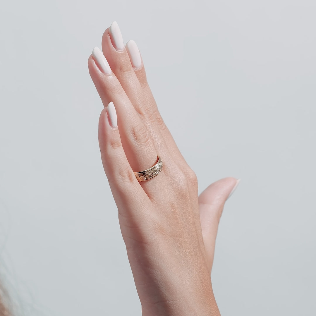 Elegant hand wearing a 6mm 10K Yellow Gold Hand Engraved Wedding Band with leaf motifs.