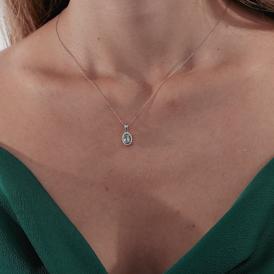 Dainty 14K yellow gold necklace featuring a natural blue topaz surrounded by diamonds, worn by a model.
