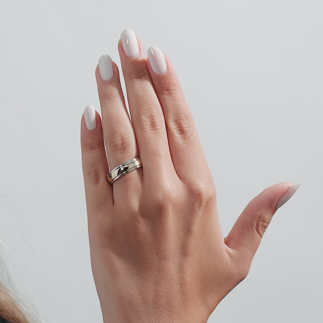 Close-up of a hand wearing a two tone gold men's wedding band, showcasing the shiny finish and comfort fit.