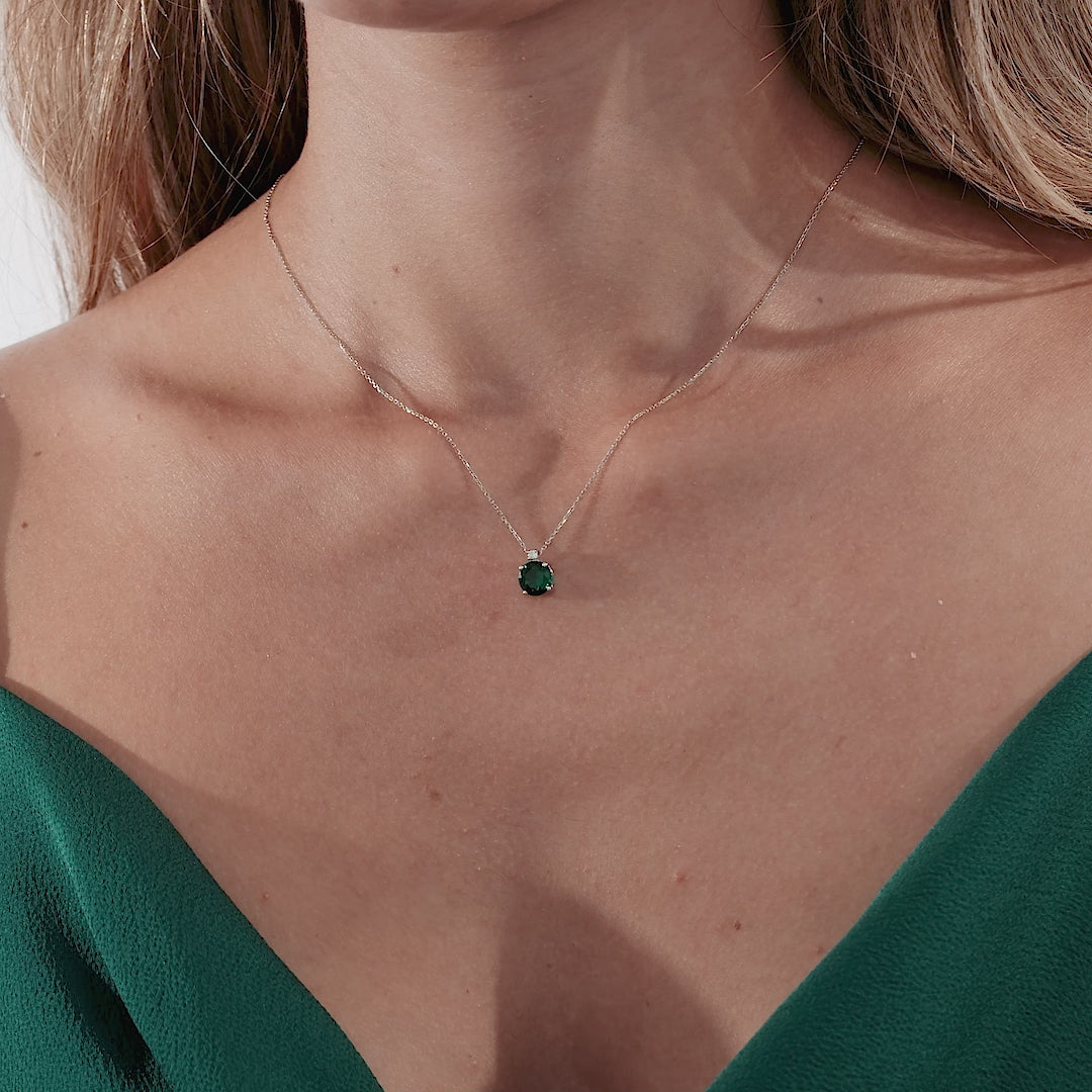 Model wearing a 14K yellow gold emerald solitaire necklace on a green dress, highlighting its delicate design.