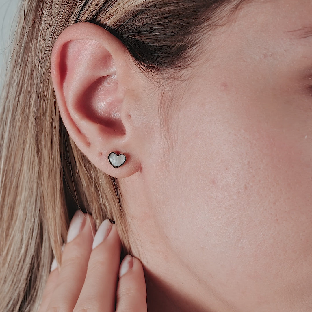 14K yellow gold minimalist heart stud earrings featuring natural mother of pearl, worn by a woman.
