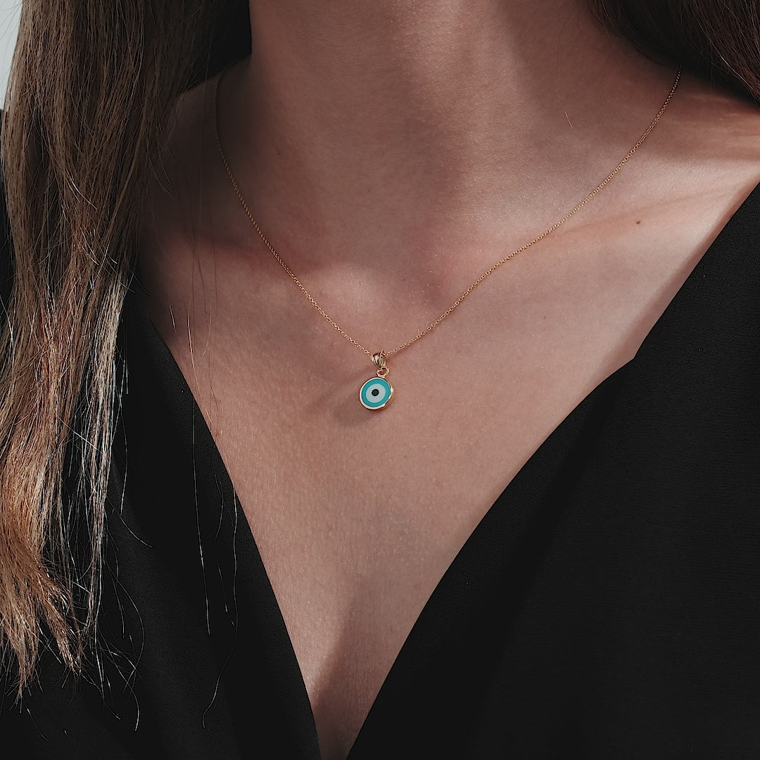 14K solid yellow gold evil eye necklace worn by a woman, featuring a delicate round pendant on a slim chain.