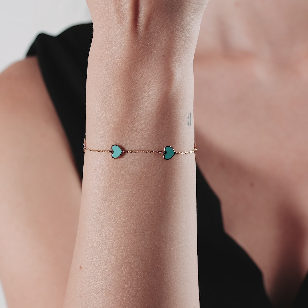 14K yellow gold turquoise heart bracelet worn on wrist, displaying two heart charms and a stylish design.