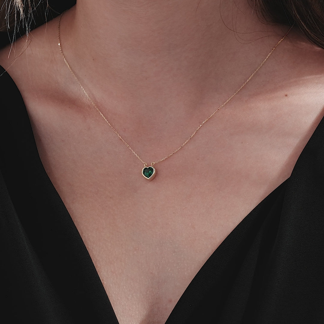 Model wearing a 14K yellow gold heart shape solitaire emerald necklace with a delicate chain.