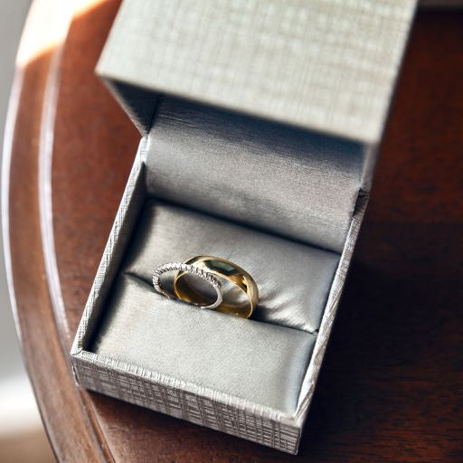 Elegant wedding rings in a gray jewelry box placed on a wooden surface, symbolizing love and commitment.