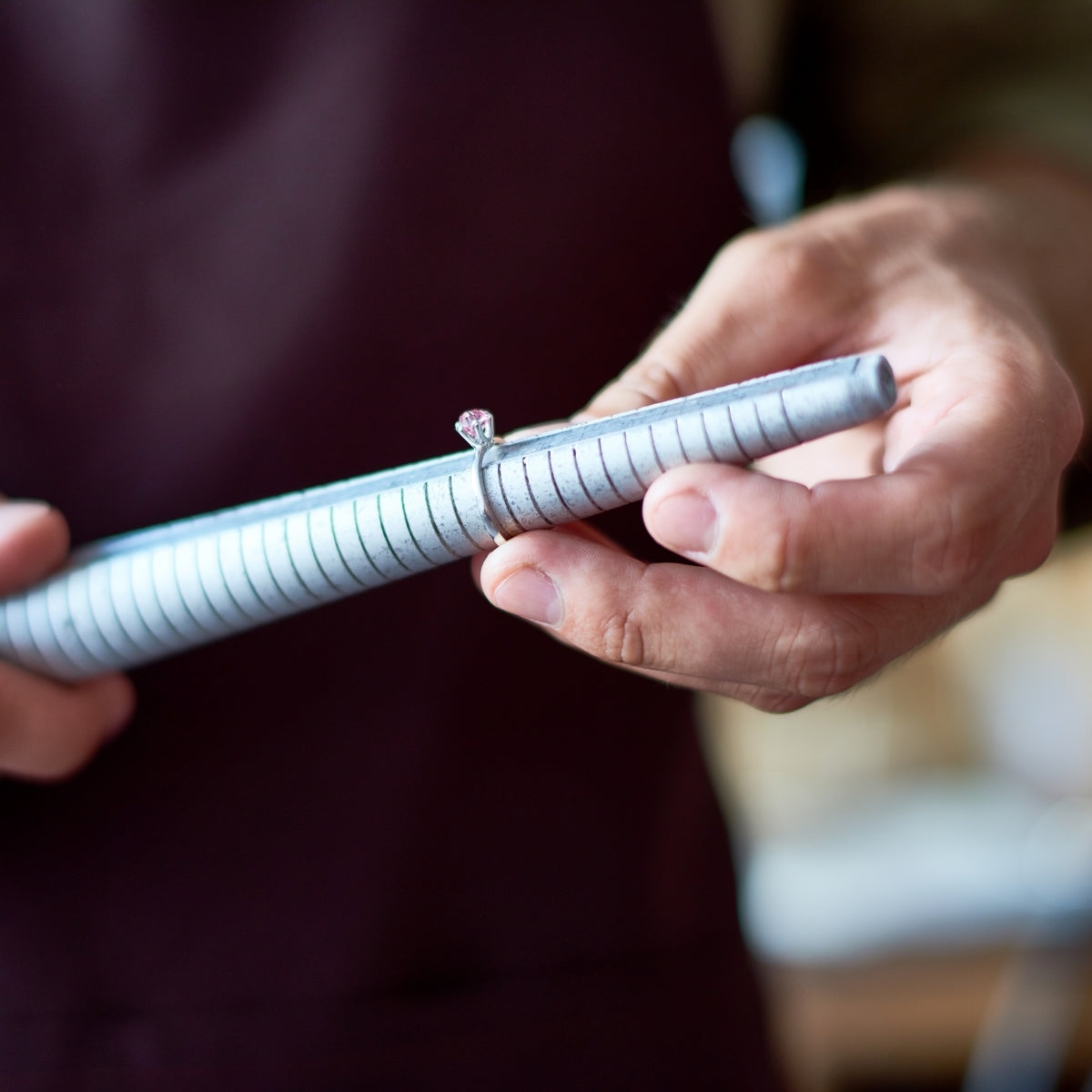 Jeweler holding a ring sizer tool with a diamond ring, showcasing craftsmanship and attention to detail.