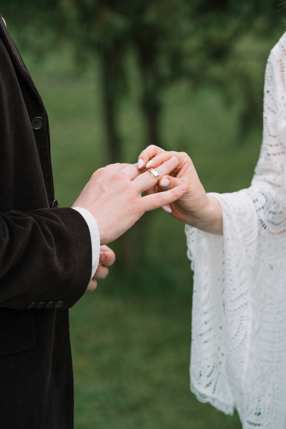 Couple exchanging wedding rings outdoors, symbolizing love and commitment in a beautiful natural setting.