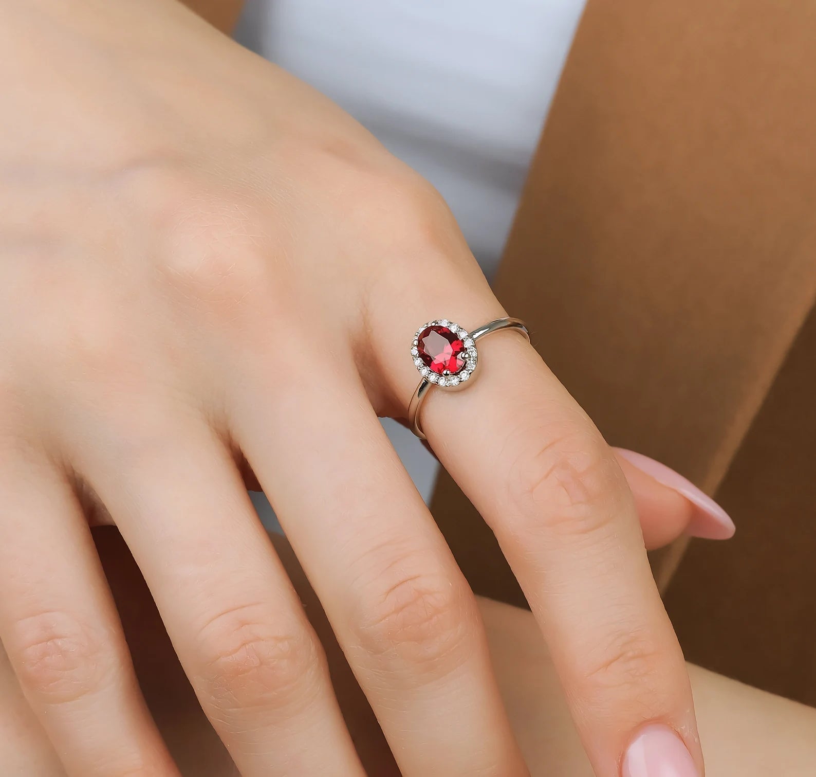 14K gold engagement ring featuring a 1 carat oval ruby surrounded by round diamonds on a woman's hand.