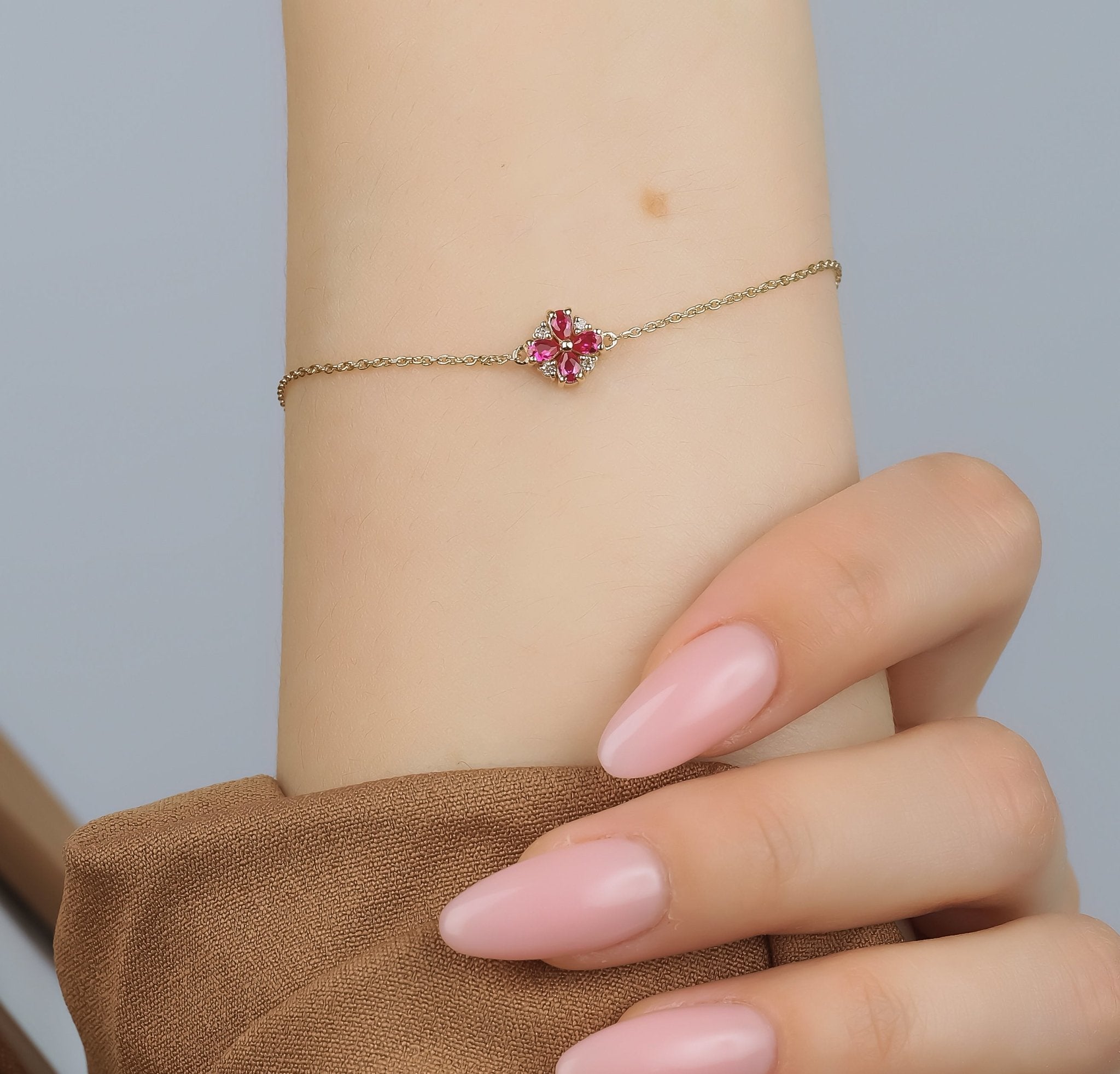 14K gold bracelet featuring pear shape ruby and diamond, worn on a hand with pink nails, perfect for elegant occasions.