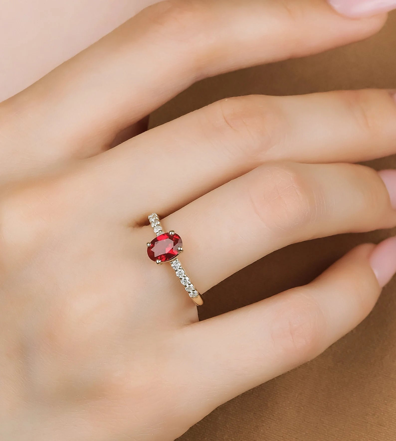 14K gold oval ruby engagement ring with diamonds on a hand, showcasing a delicate and classy design.