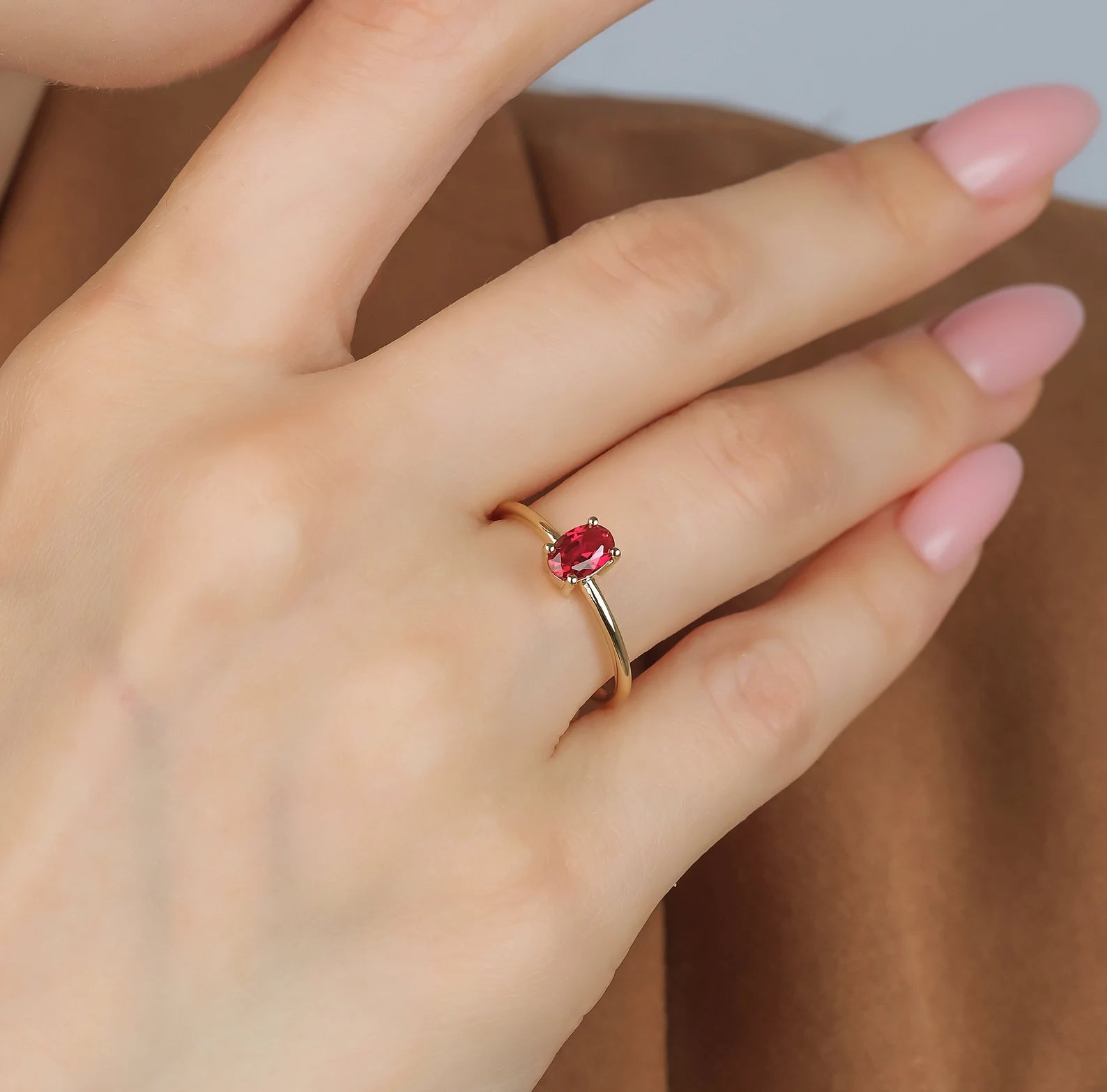 Dainty 14K gold ruby solitaire engagement ring on a hand, featuring a 0.50 carat oval ruby and shiny finish.