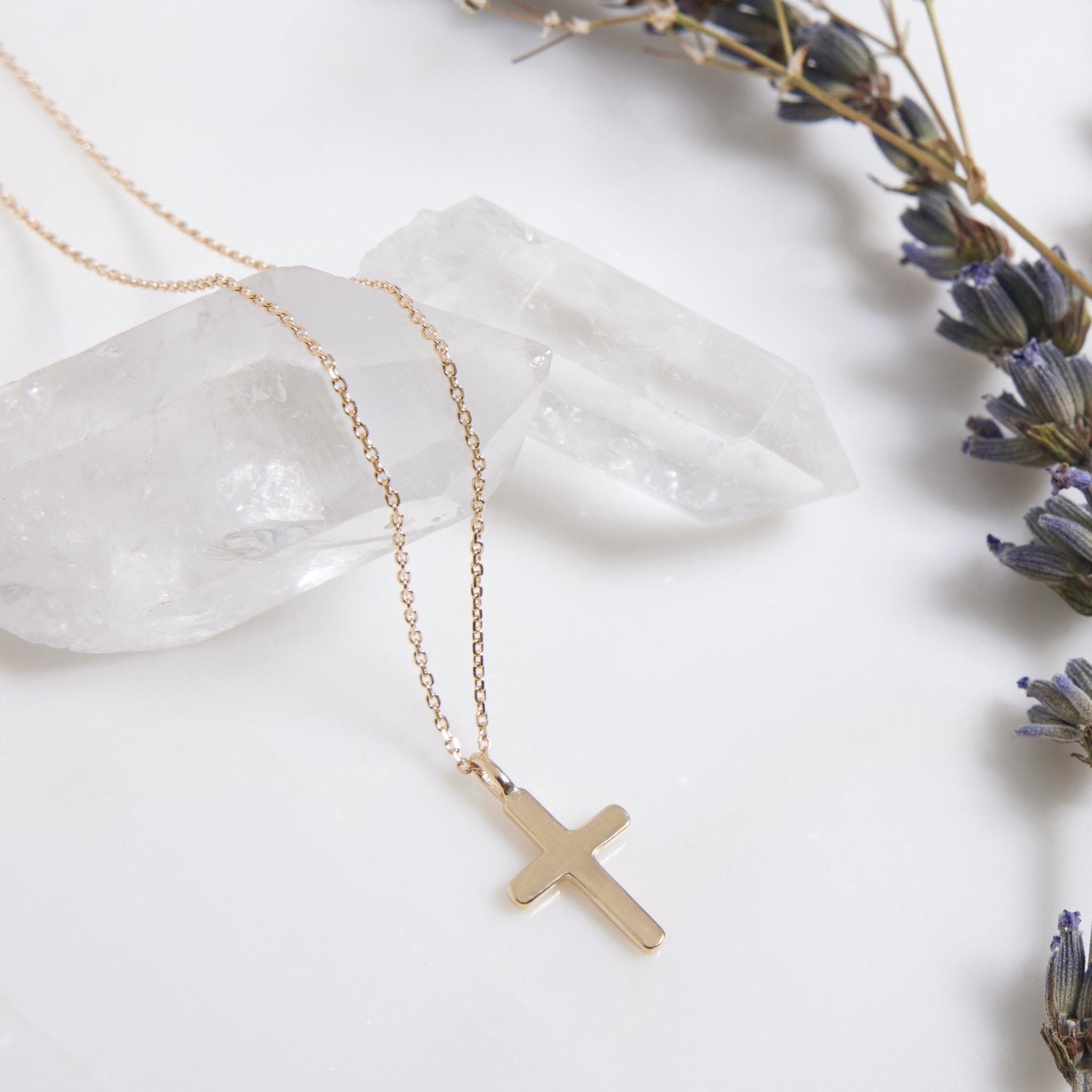 14K minimalist cross necklace on a crystal surface, showcasing dainty gold design for elegant style.