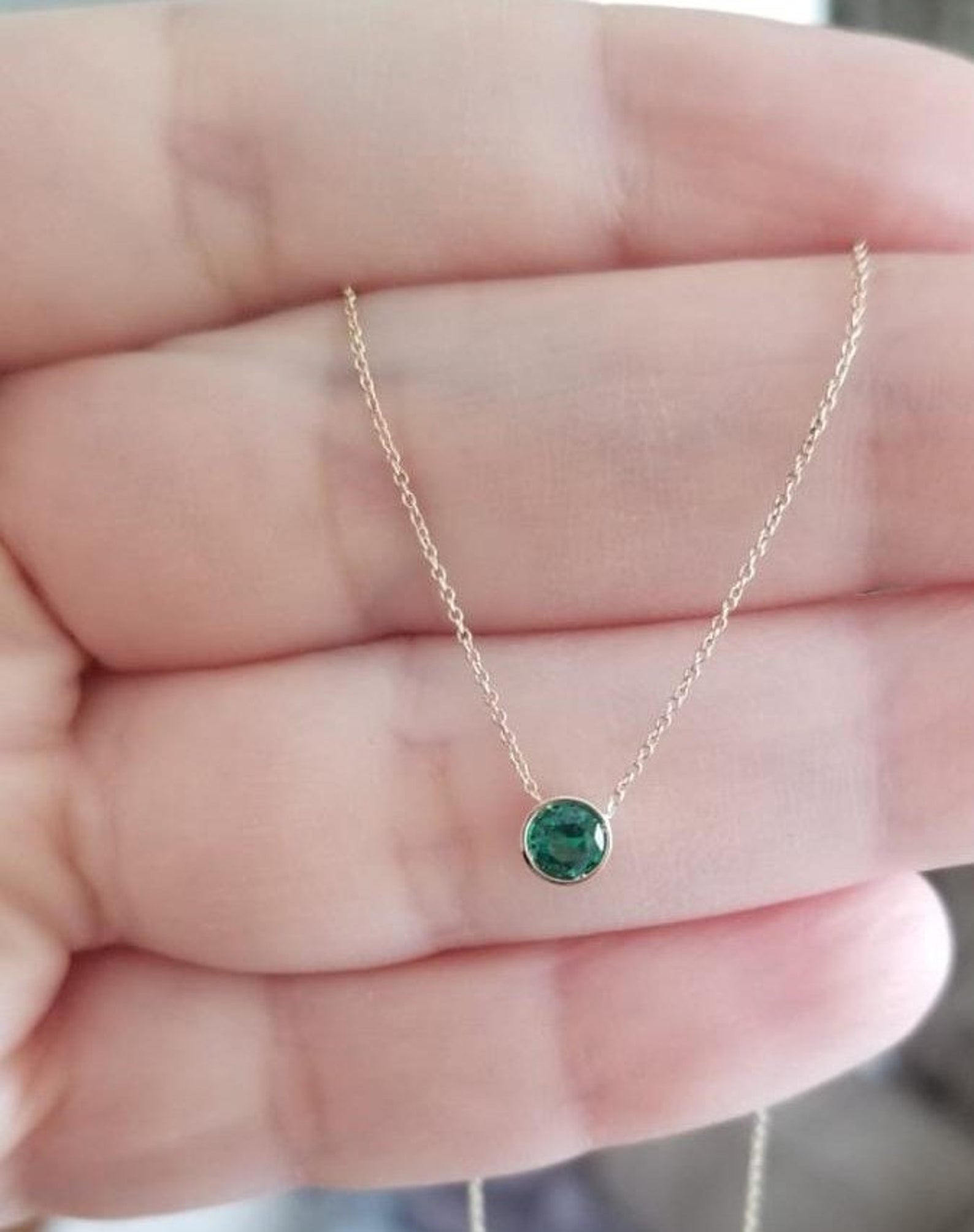 14K solid white gold 4mm bezel set solitaire emerald necklace held in a hand, showcasing its dainty design.