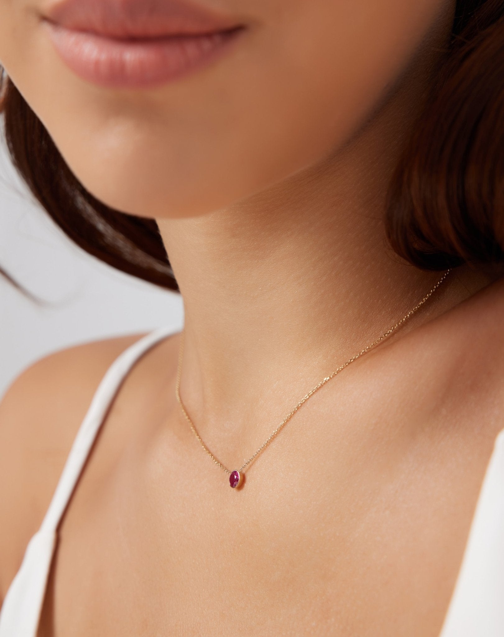 Close-up of a woman wearing a 14K white gold bezel set 4mm ruby solitaire necklace, showcasing its delicate design.