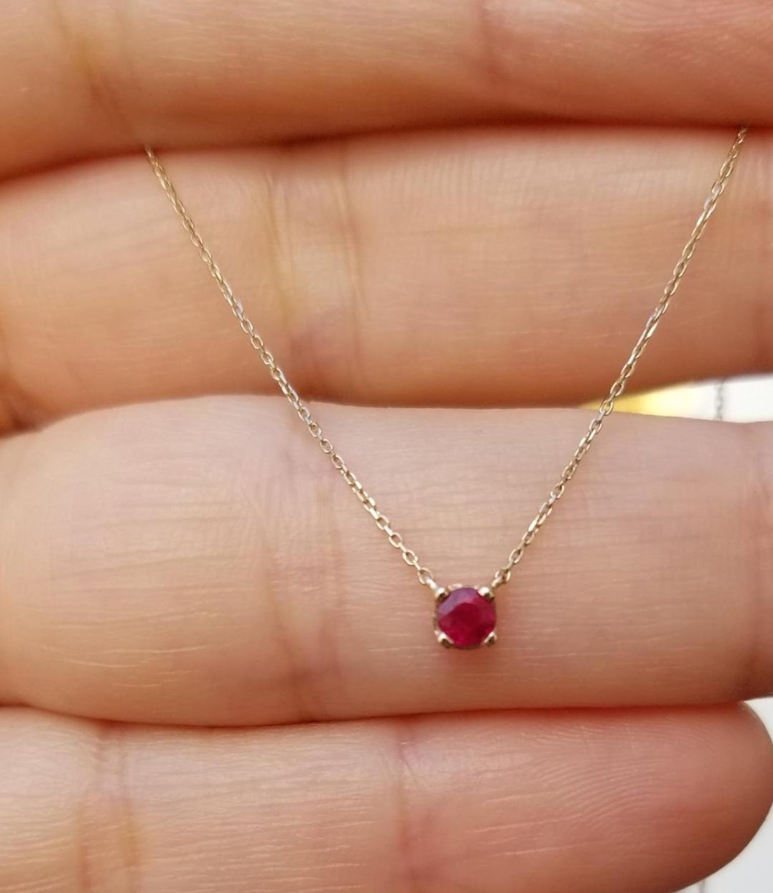 Dainty 14K white gold solitaire ruby necklace in prong setting held in hand, featuring a 5mm lab-created ruby.