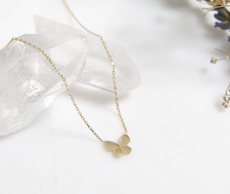 14K solid yellow gold dainty butterfly necklace displayed on crystal, highlighting minimalist design and elegance.