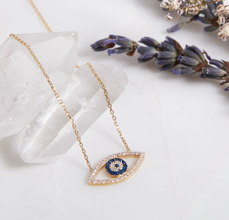 14K solid yellow gold minimalist evil eye necklace with CZ and blue stone on a crystal backdrop.