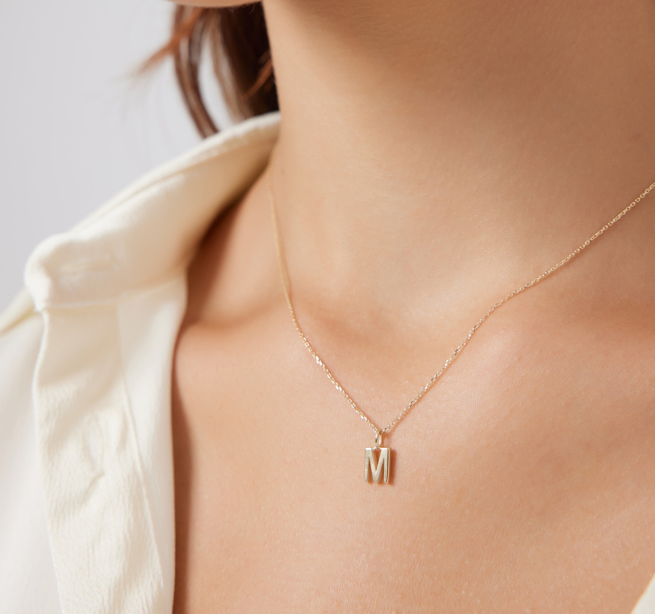 14K solid yellow gold initial necklace featuring letter M, worn on a model's neck.