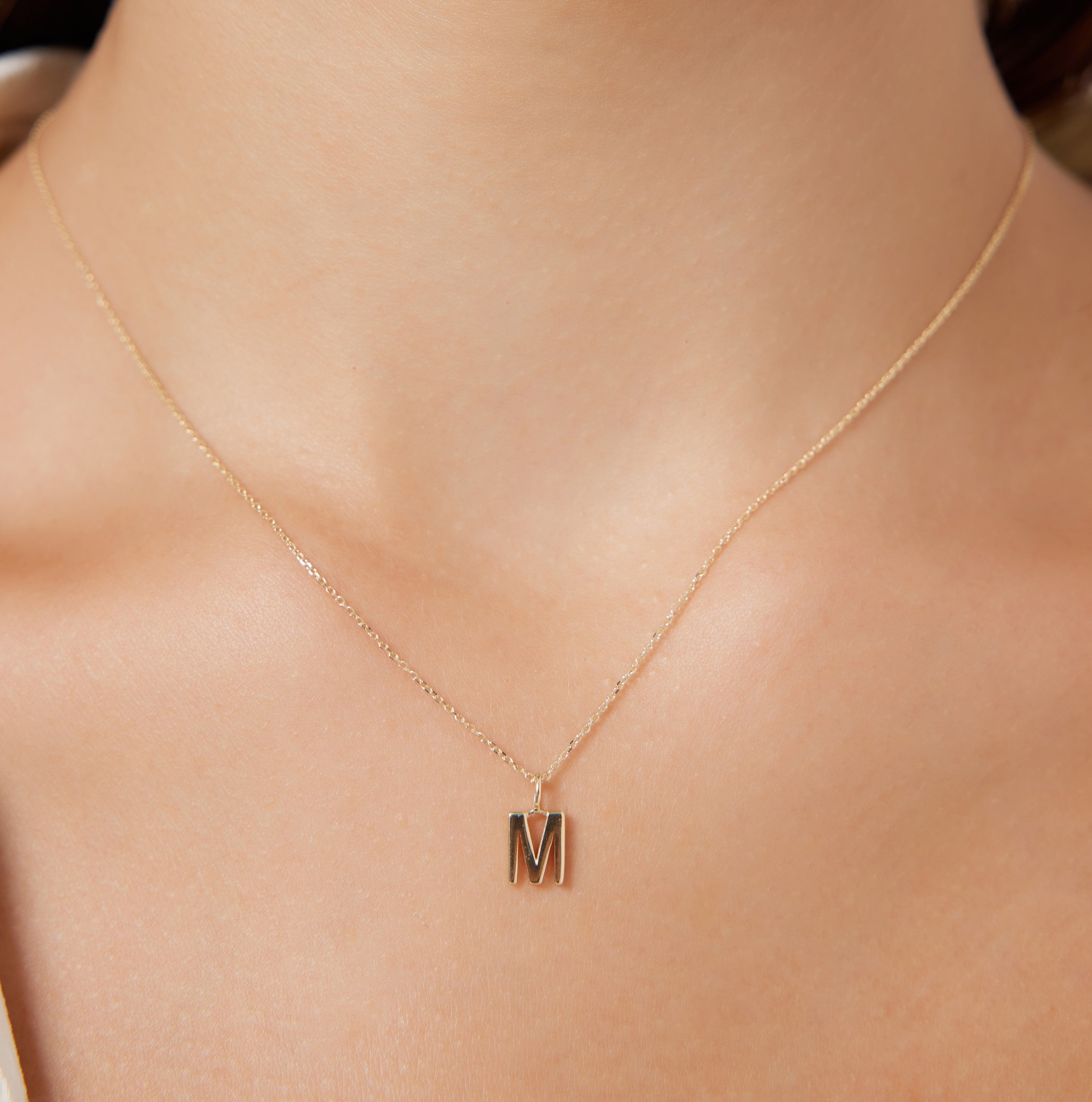 14K solid yellow gold initial necklace featuring the letter M, dainty design, worn on a woman's neck.