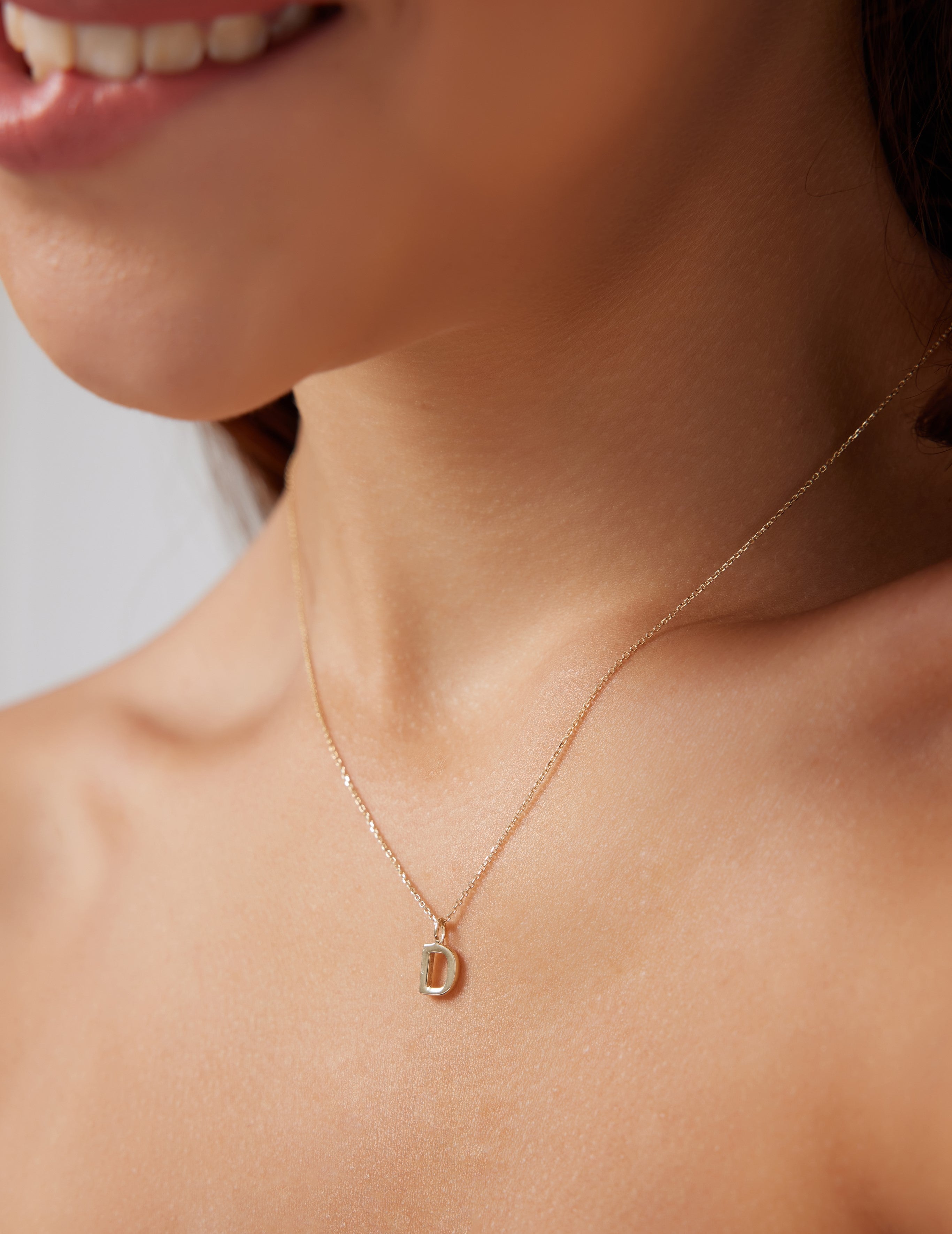 Model showcasing a dainty 14K solid yellow gold initial necklace featuring the letter D, 16 inches long.