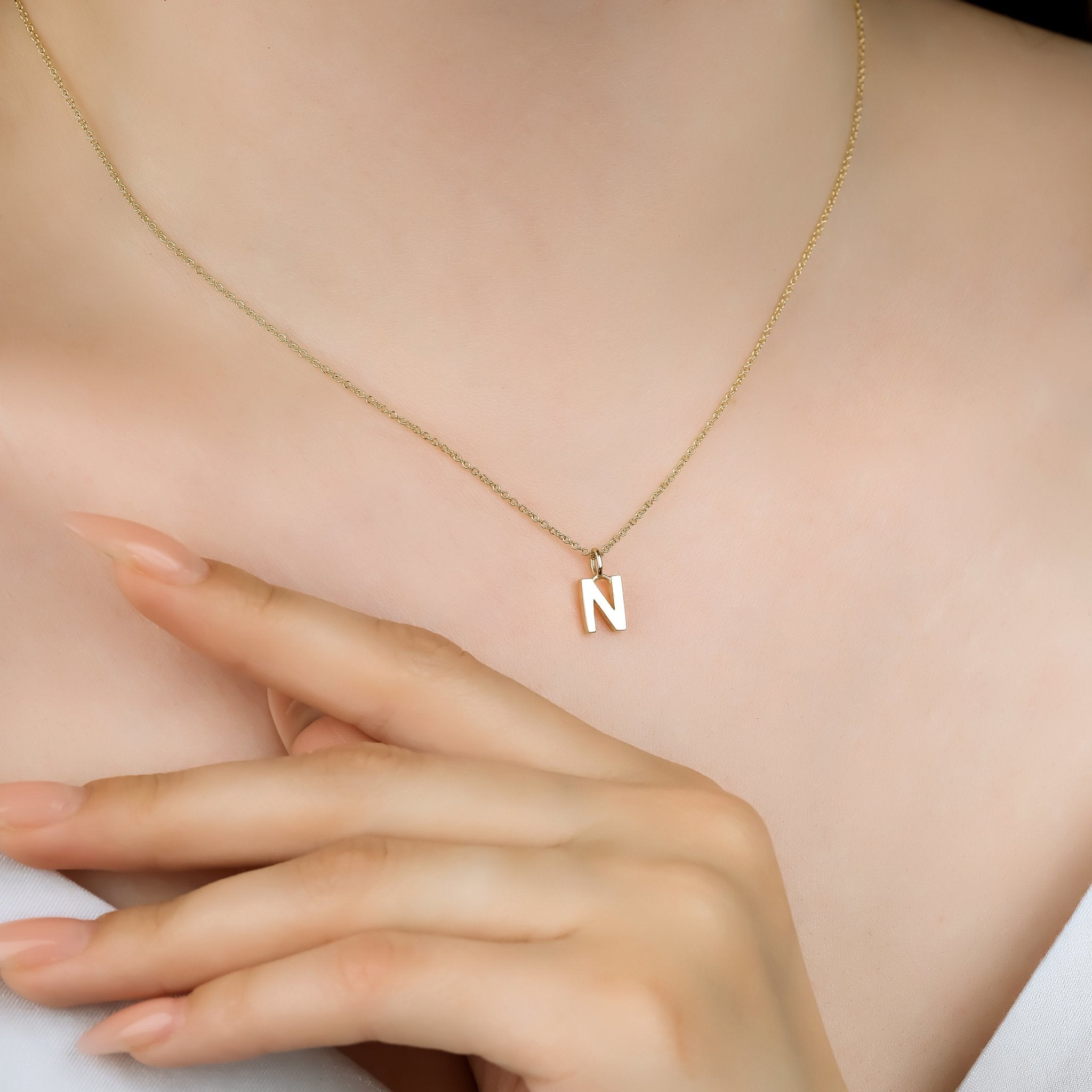 14K solid yellow gold initial necklace featuring the letter N, worn on a woman, highlighting the dainty design.