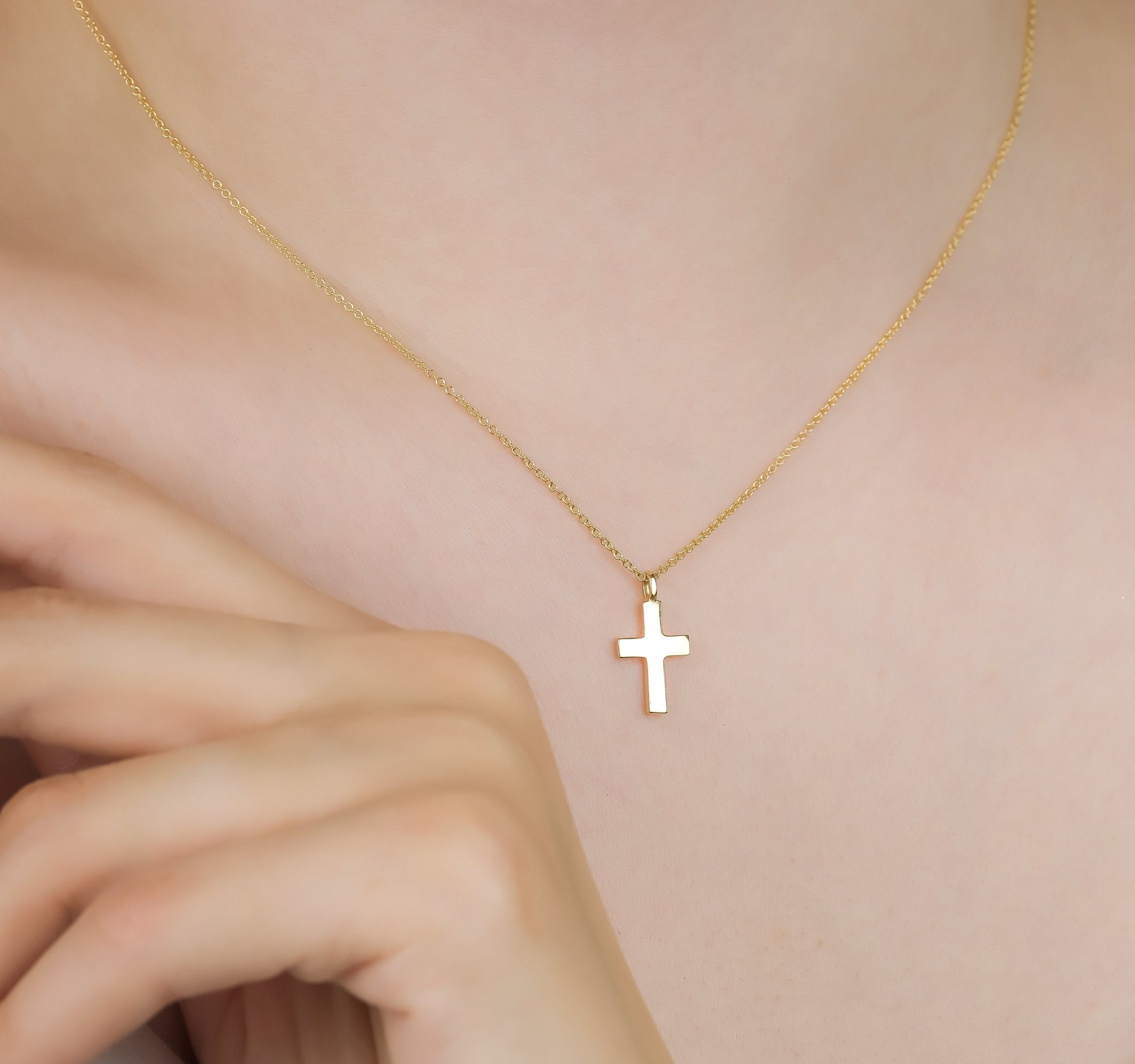 14K solid yellow gold dainty cross necklace worn by a woman, minimalist design, 16 inch chain with an 18mm cross.