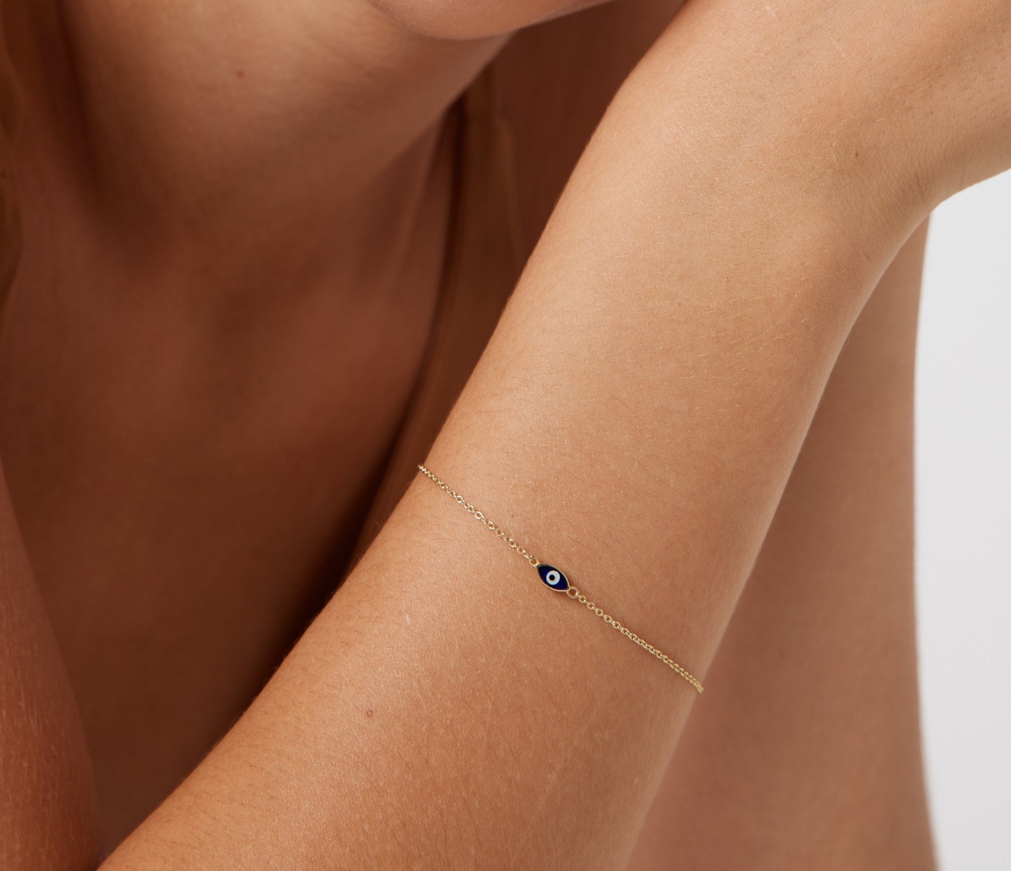 Dainty 14K solid yellow gold minimalist evil eye bracelet worn on a woman's wrist, showcasing a dark blue eye design.