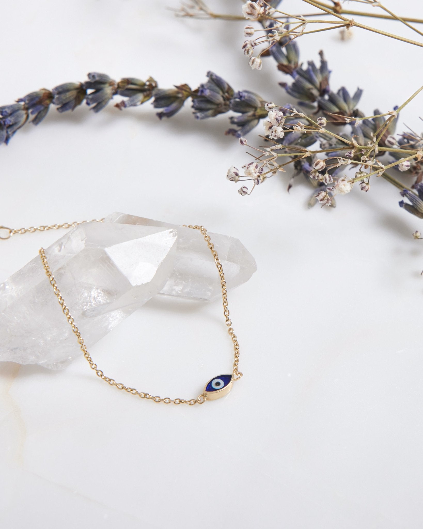 14K solid yellow gold minimalist evil eye bracelet with dark blue enamel placed on a crystal and dried flowers.