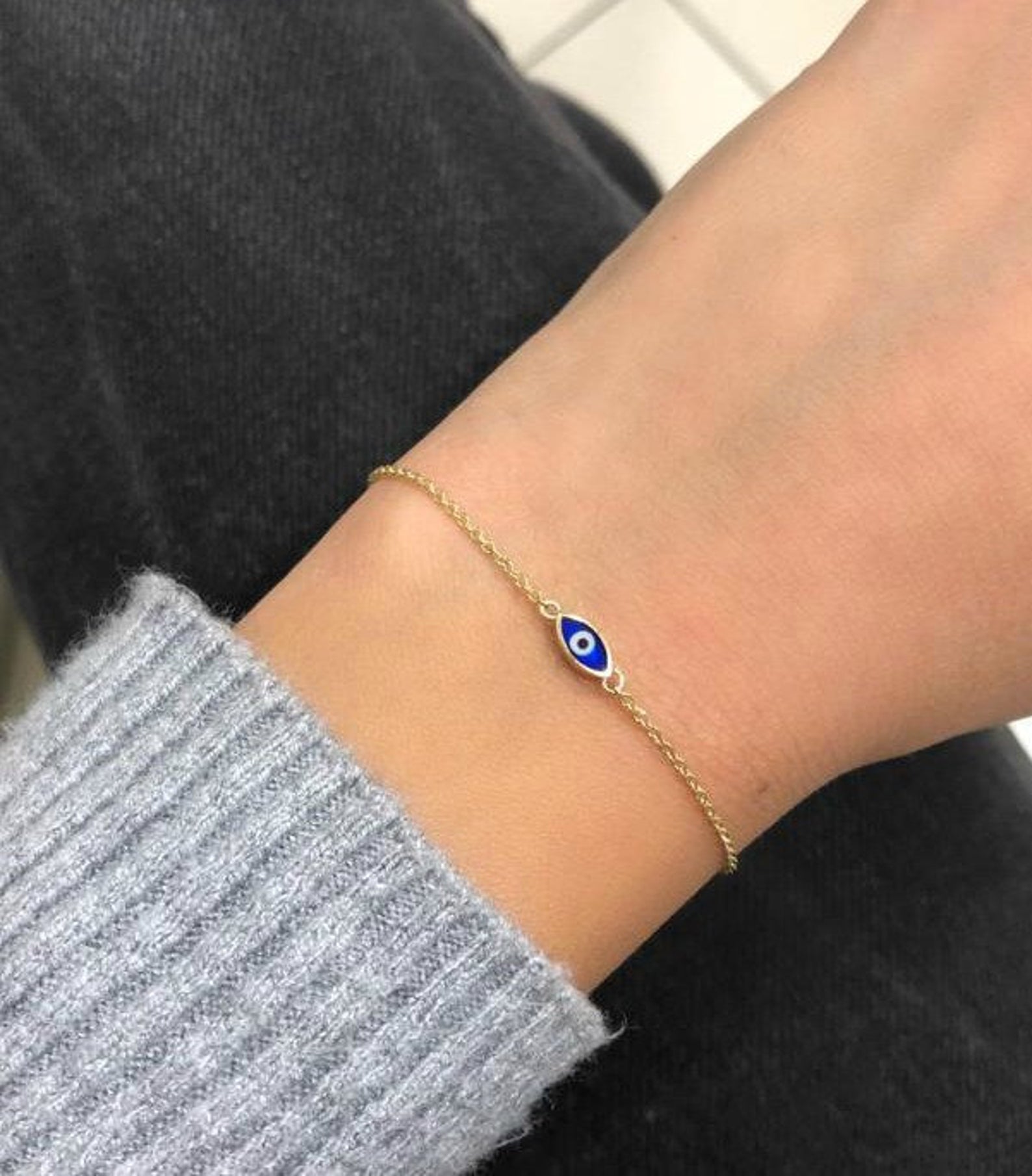 14K solid yellow gold minimalist evil eye bracelet worn on wrist with dark blue eye detail.