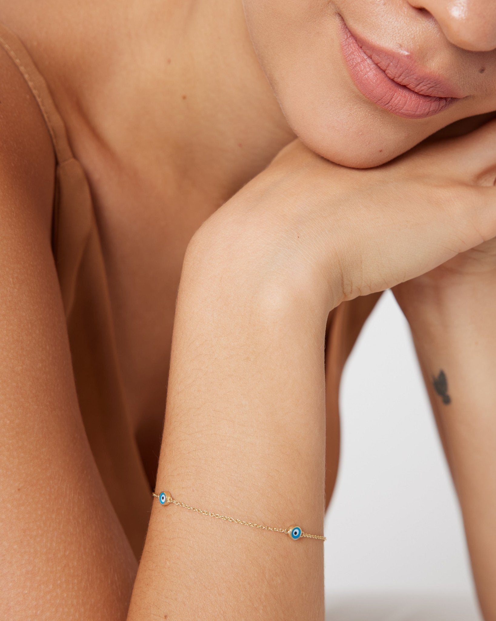 Dainty 14K solid yellow gold evil eye bracelet worn on a woman's wrist, showcasing minimalist design with blue eye detail.