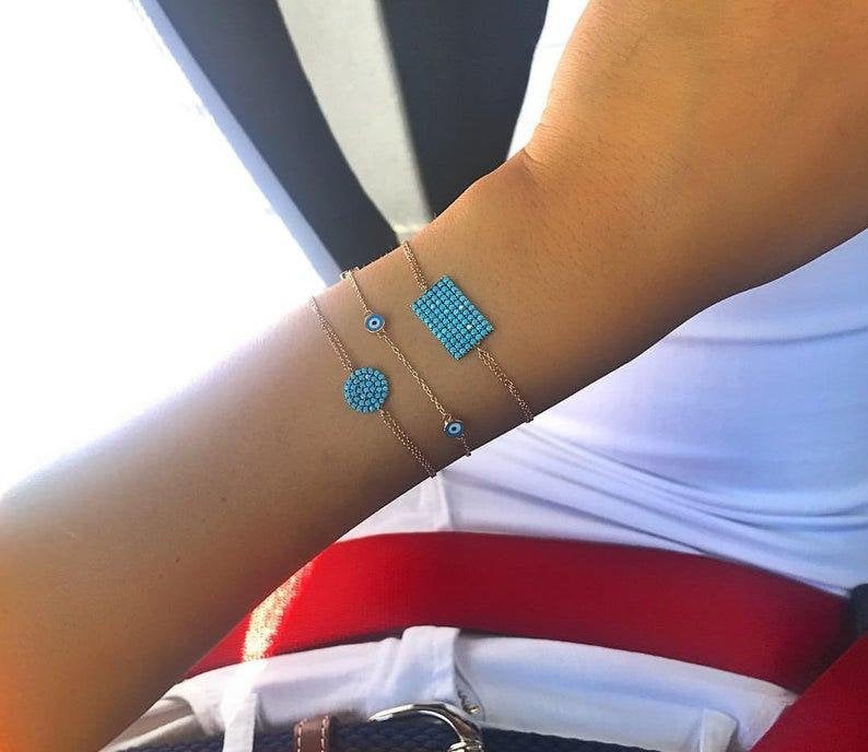 Minimalist turquoise evil eye bracelets on a woman's wrist, featuring dainty gold chains and geometric designs.