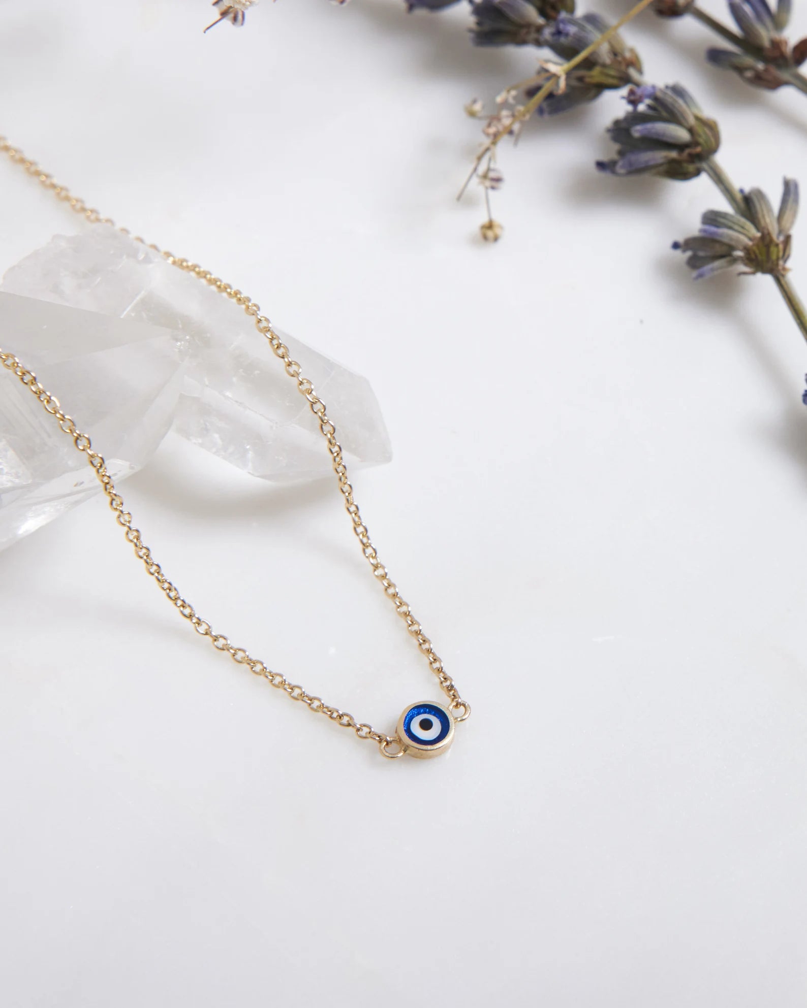 14K solid yellow gold evil eye necklace with dark blue pendant on display with lavender flowers.