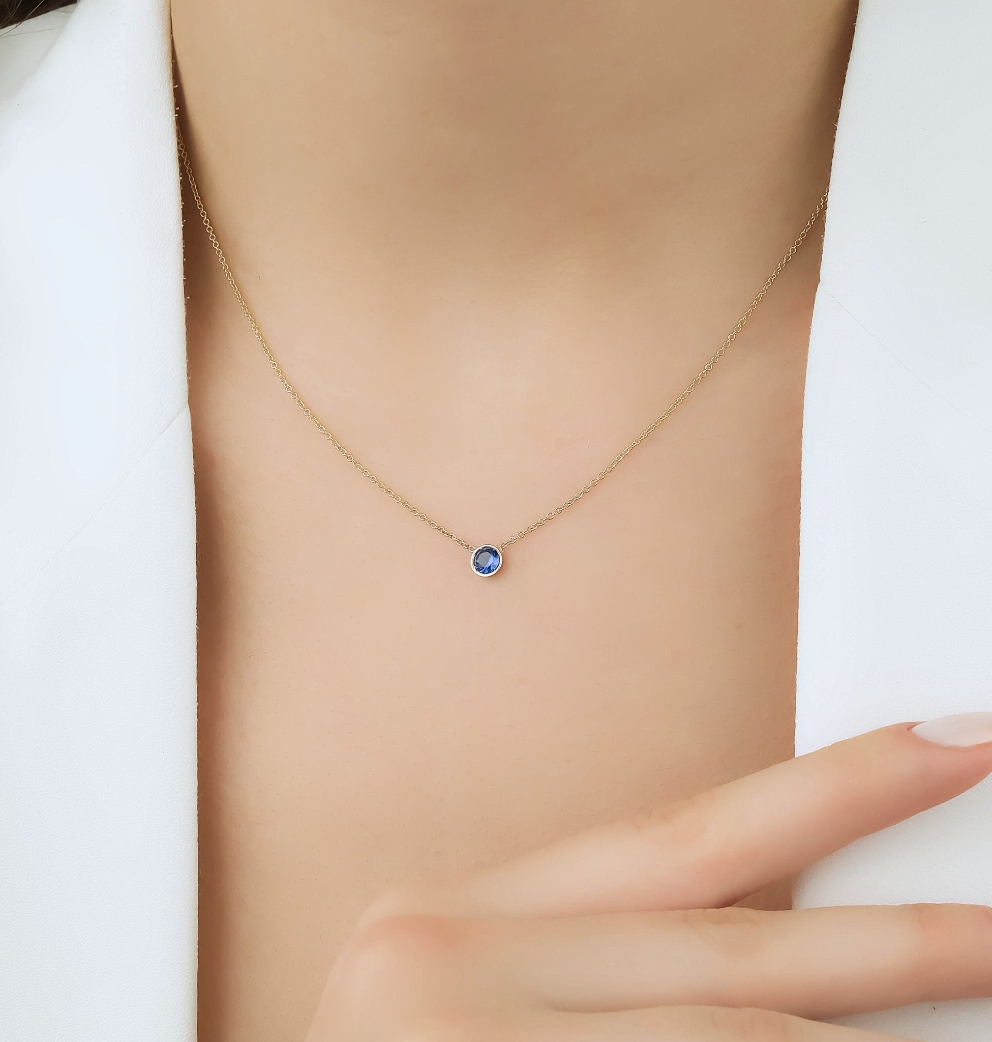 14K yellow gold 4mm bezel set solitaire sapphire necklace worn by a model, showcasing minimalist elegance.