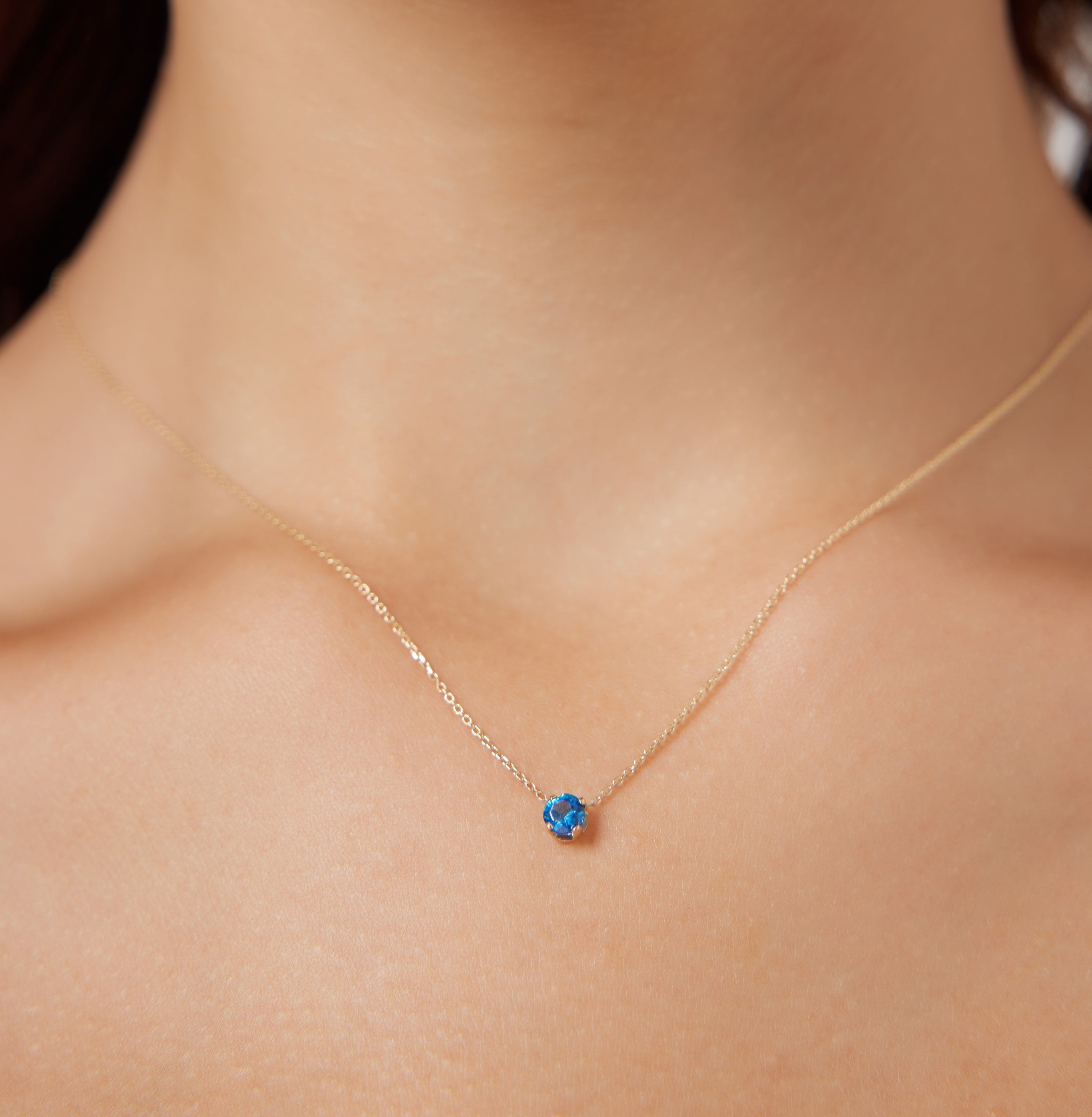Minimalist 14K yellow gold 5mm prong setting solitaire sapphire necklace worn on the neckline.