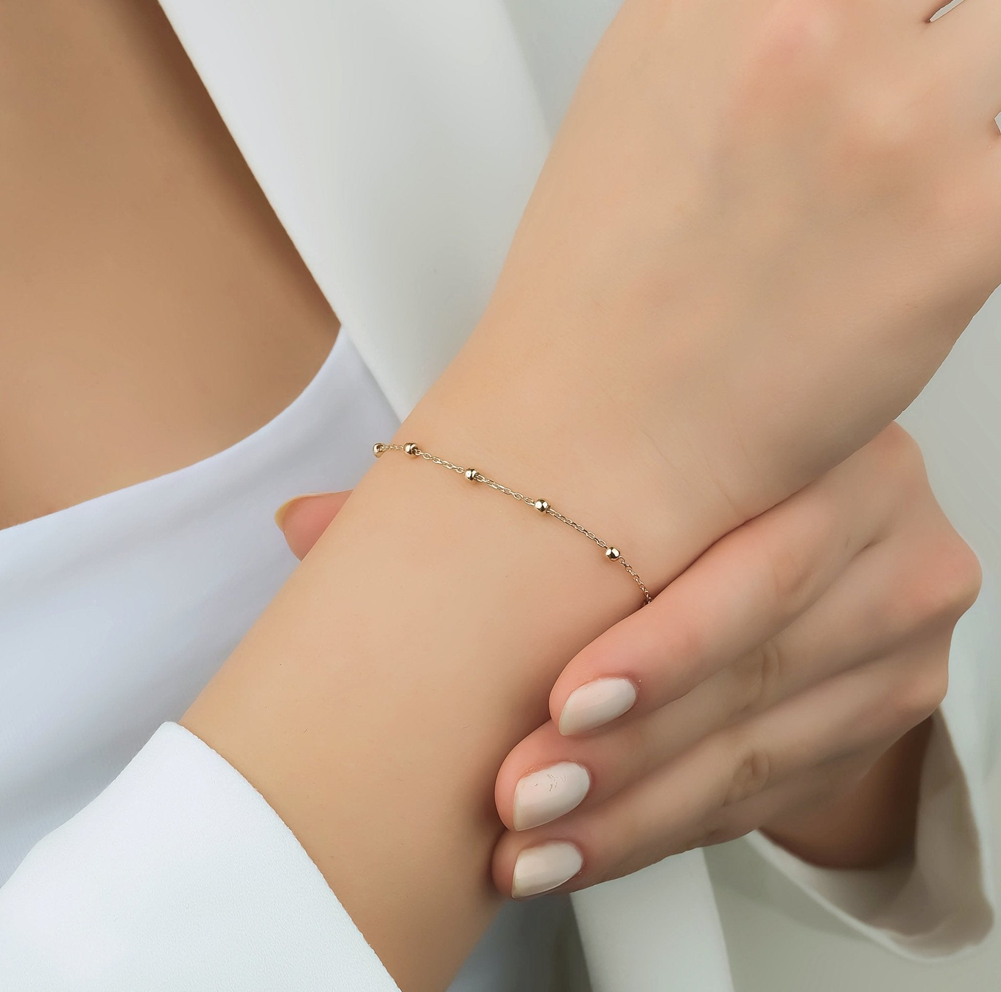 14K solid yellow gold station ball bracelet worn on a woman's wrist, elegant design with small gold beads.