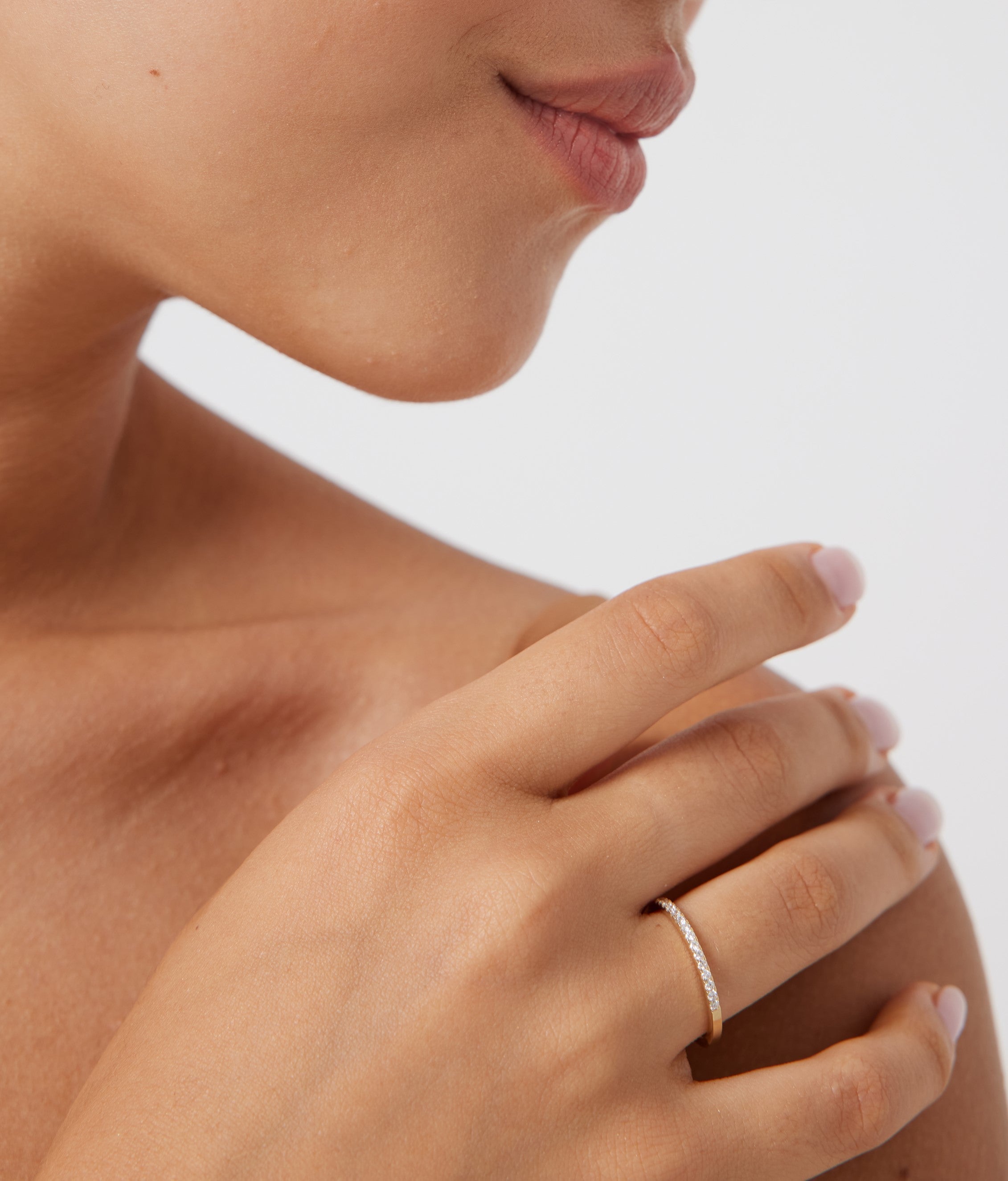 Close-up of a hand wearing a 14K yellow gold women's diamond wedding band featuring 15 round diamonds.