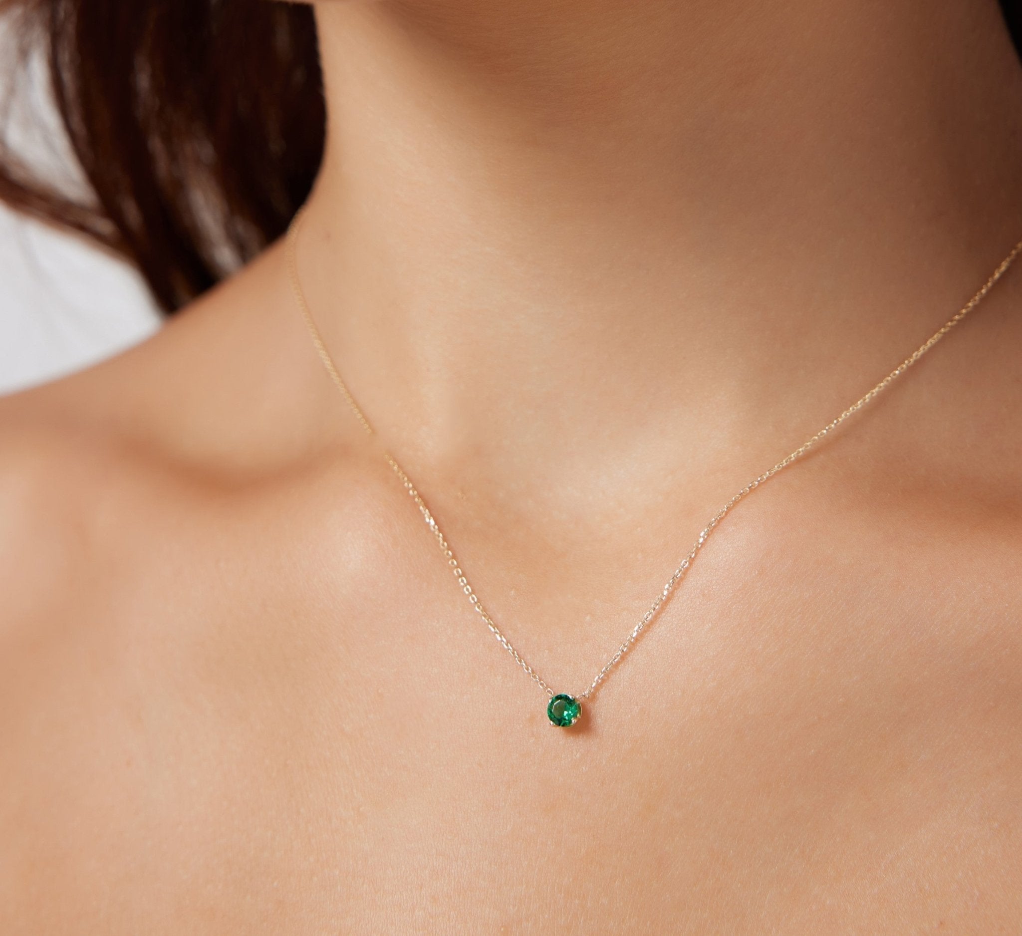 Dainty 14K white gold minimalist necklace featuring a 5mm prong set emerald pendant on a model's neck.